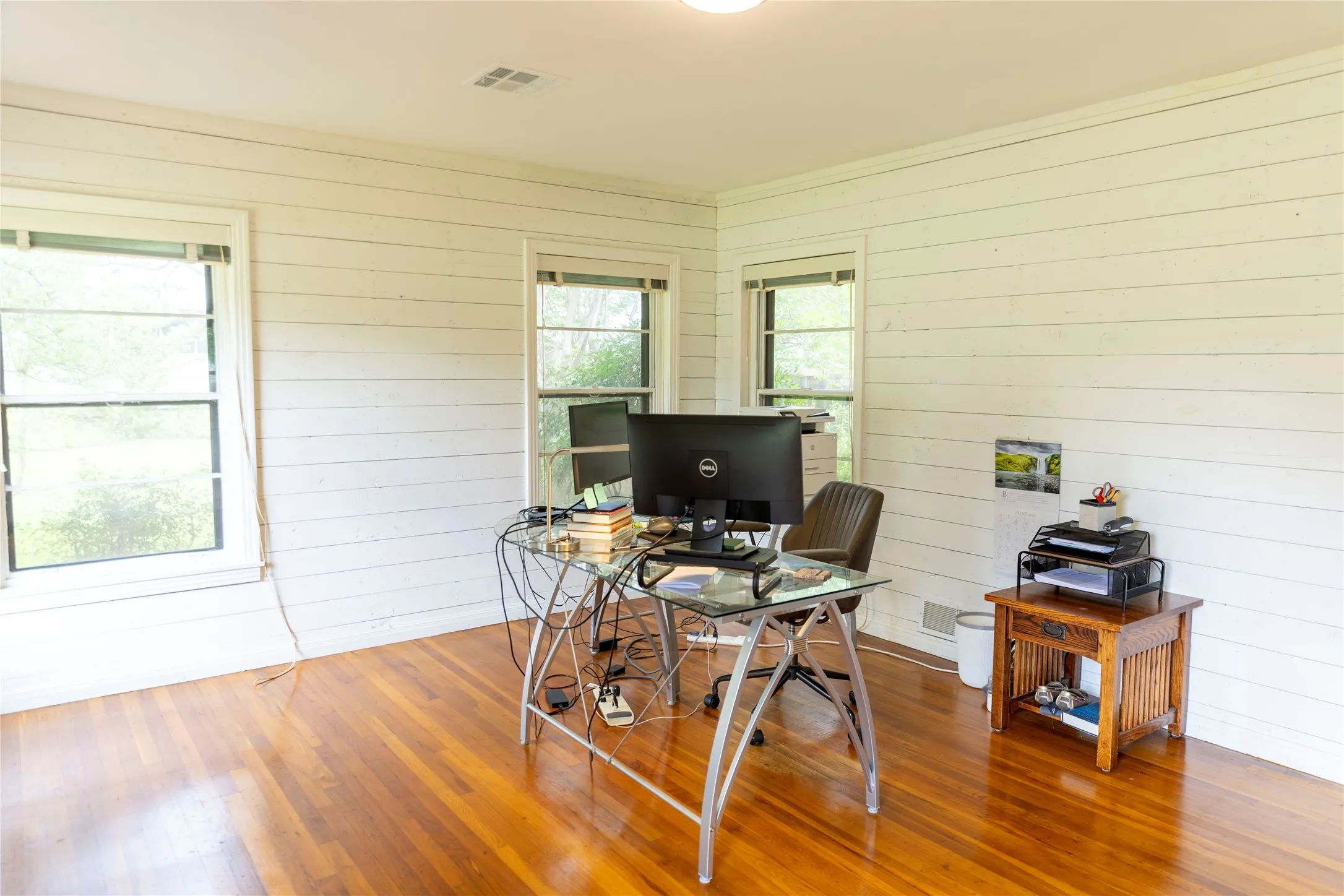 Room featuring wood-finish flooring, two large windows, white shiplap walls, and a recessed ceiling light fixture