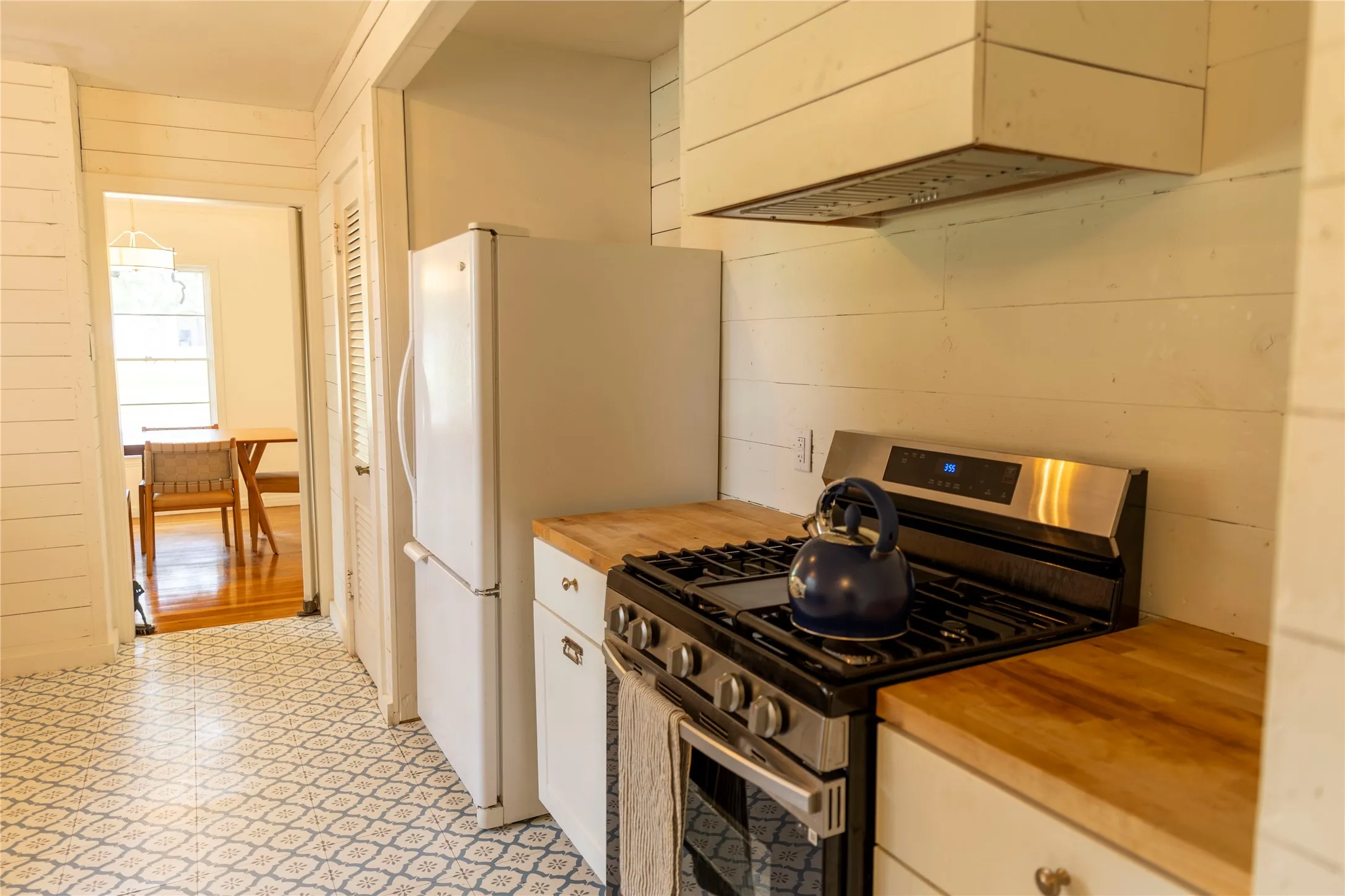 Kitchen featuring shiplap walls, wood-finish countertops, geometric-patterned floor tiles, and a stainless steel oven range with an overhead exhaust hood