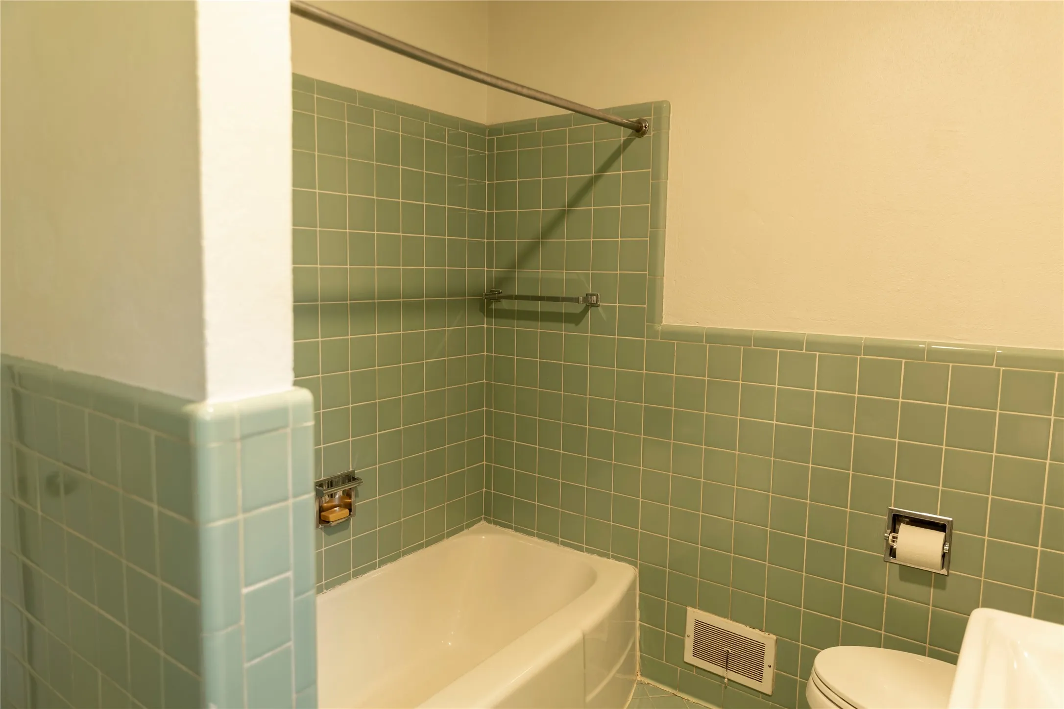Bathroom featuring a white bathtub, green square wall tiles, and white wall paint