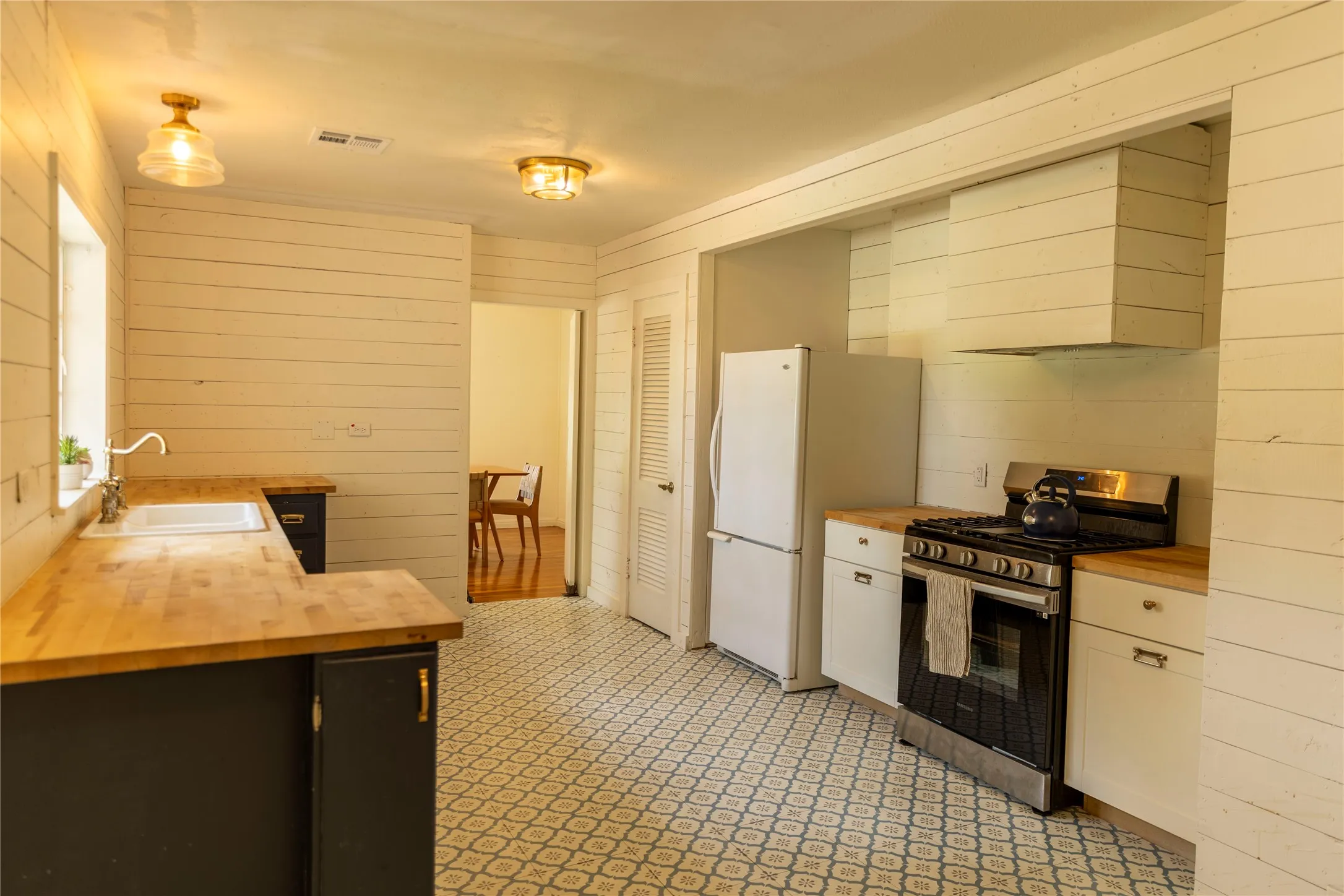 Kitchen featuring wood-finish countertops, geometric-patterned floor tile, white shiplap walls, and a built-in range with an integrated ventilation hood