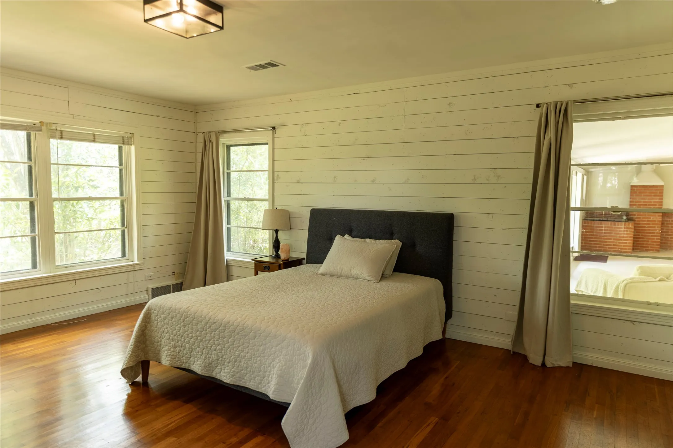 Room featuring warm-toned wood flooring, white horizontal plank wall finishes, and multiple windows providing natural light