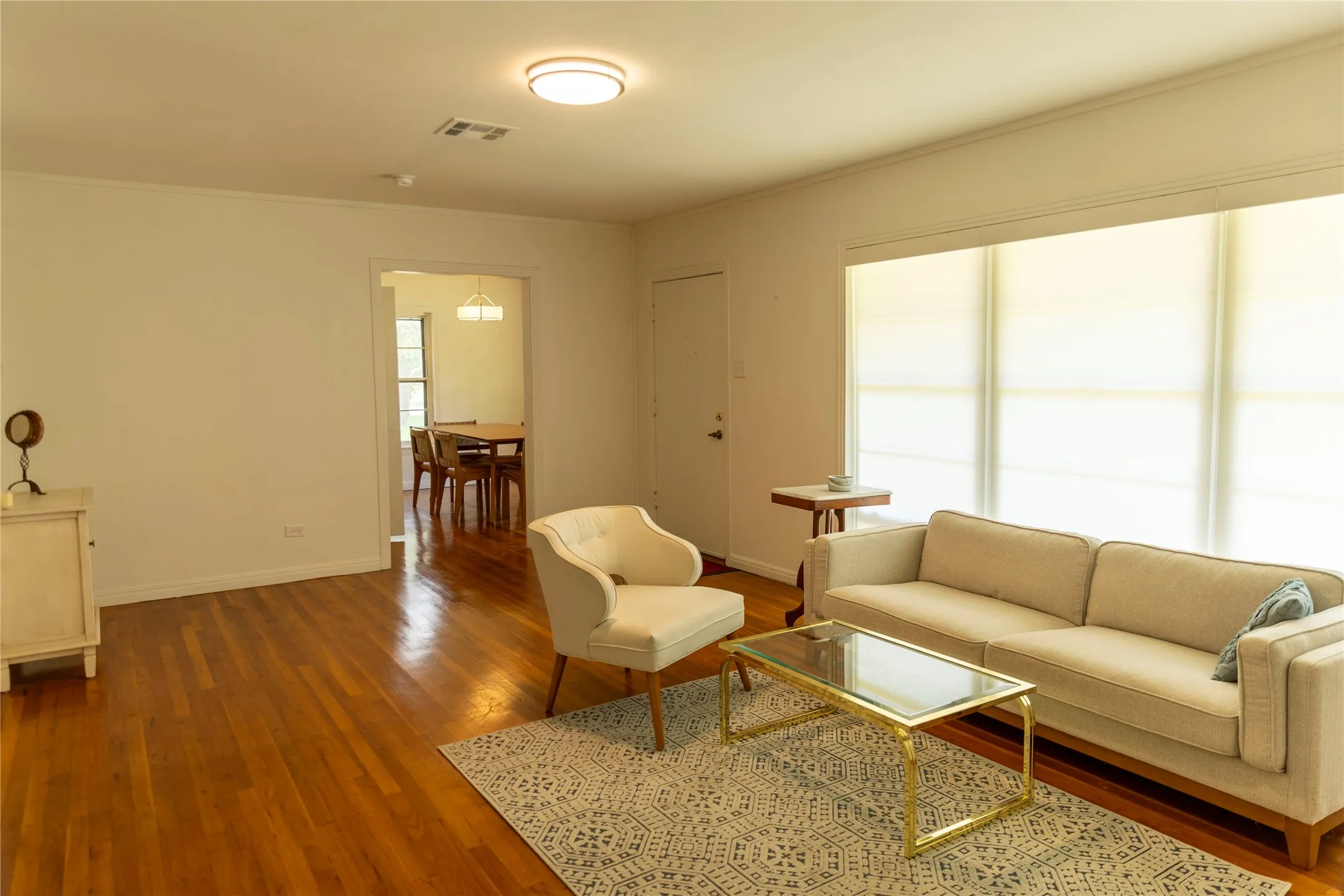 Living area featuring wood-finish flooring, a broad window with roller shades, and a flush-mount ceiling light