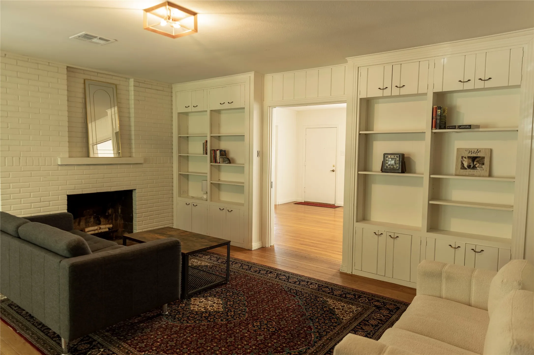 Living room featuring a brick fireplace with a mantel, extensive built-in shelving, wood-finish flooring, and a flush mount ceiling light fixture