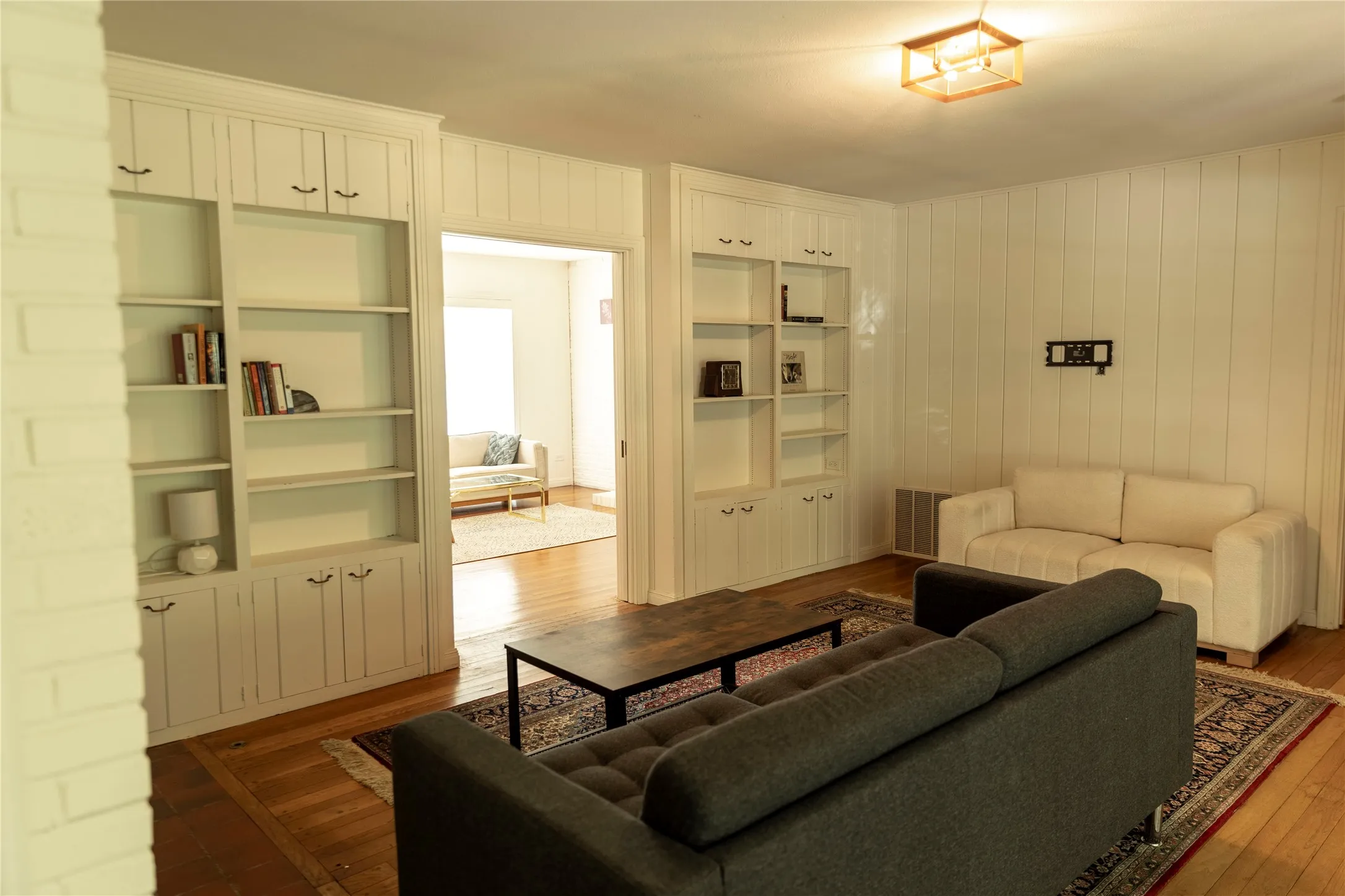Living area featuring white paneled walls, built-in shelving with lower cabinetry, and wood-finish flooring