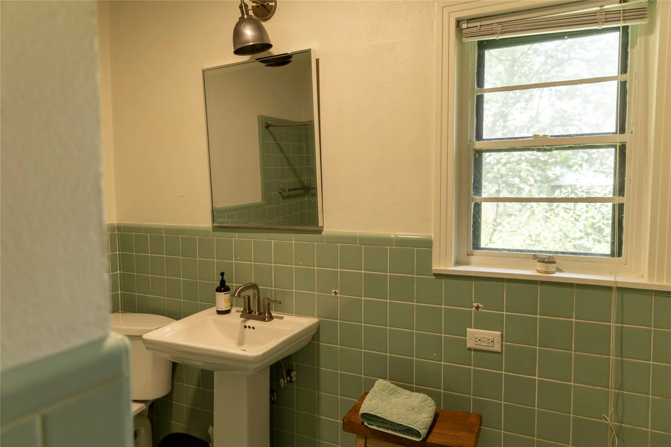 Bathroom featuring a pedestal sink with a brushed nickel faucet, a rectangular mirror, and a wall-mounted light fixture