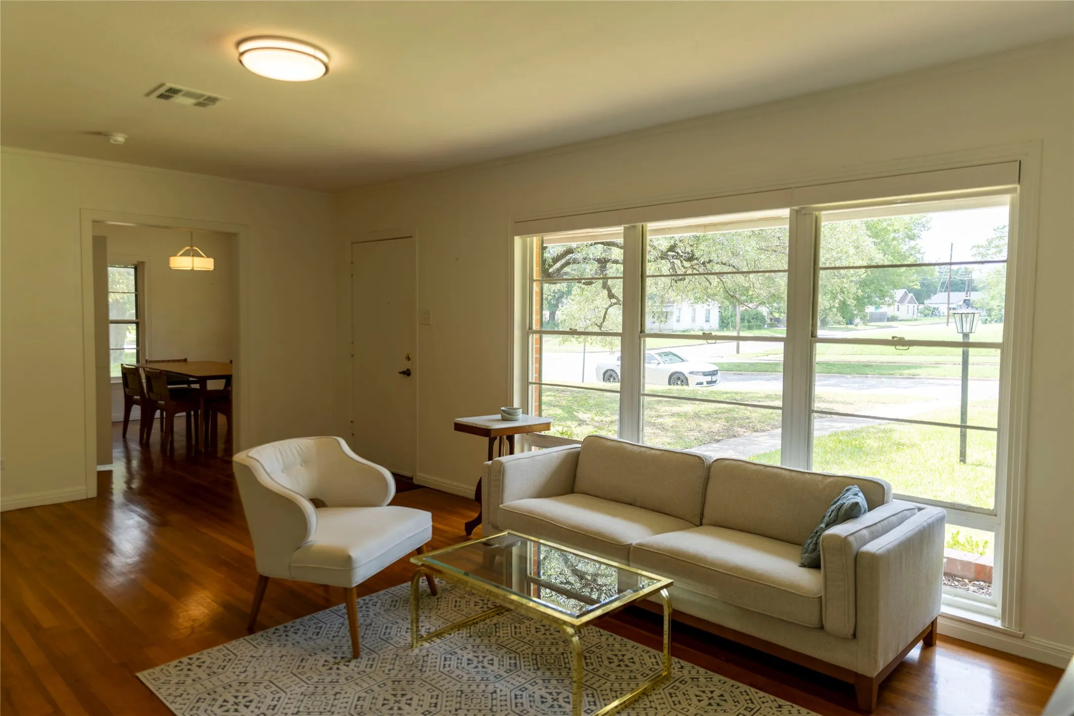 Living area featuring expansive windows, wood-finish flooring, a contemporary ceiling light fixture, and an open entryway to an adjacent room