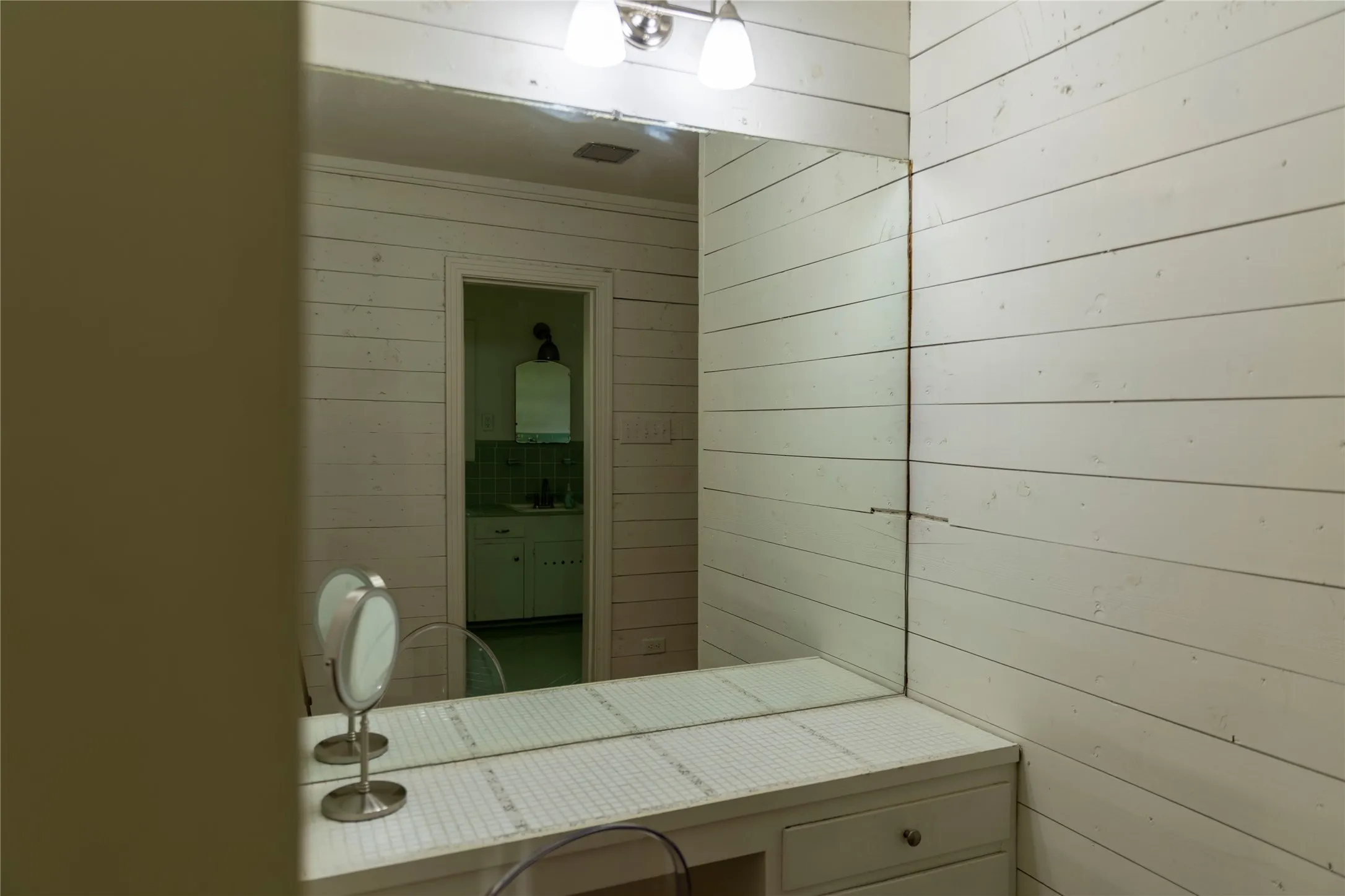 Shiplap wall paneling complementing a built-in vanity with a tiled countertop and integrated mirror