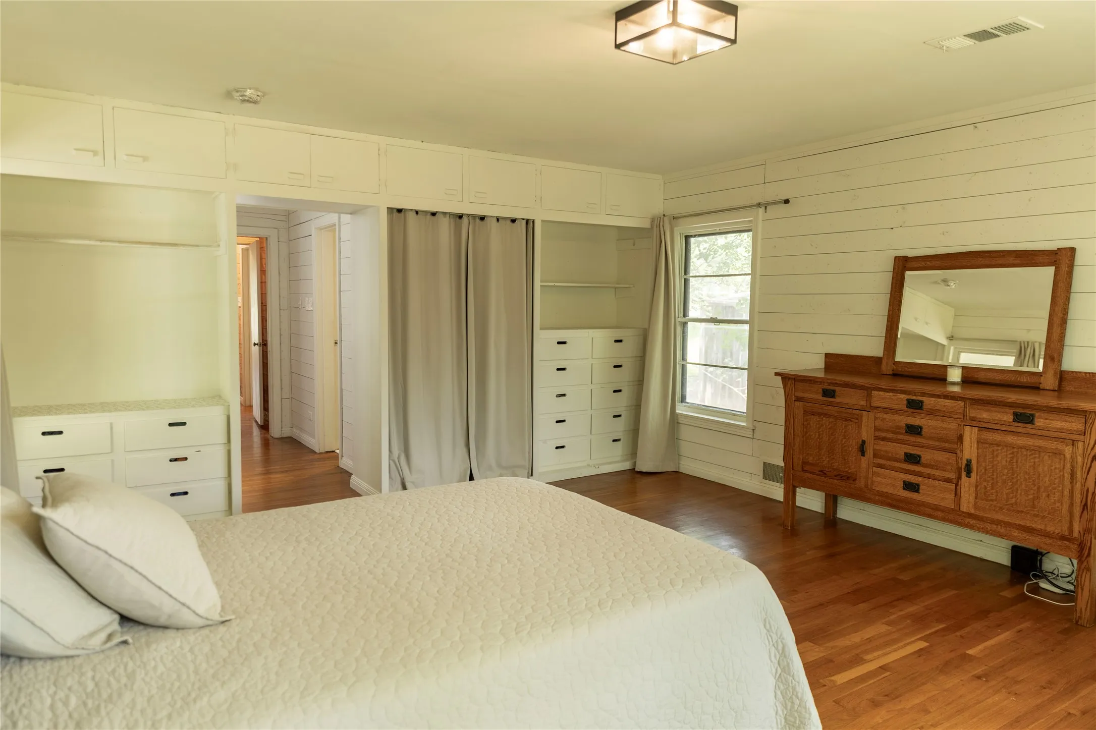 Bedroom featuring wood-finish flooring, white shiplap-style walls, built-in cabinetry, an integrated closet system with drawers and hanging space, and a ceiling-mounted light fixture