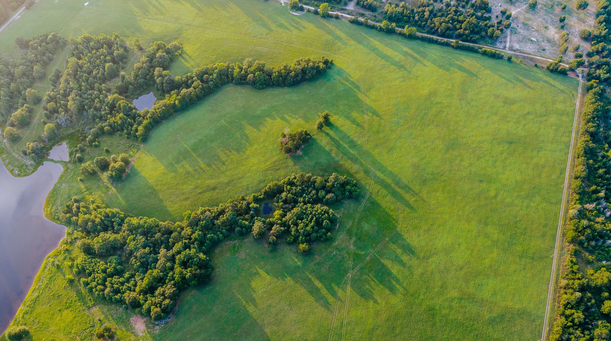 Expansive green pastures featuring wooded areas and a substantial body of water