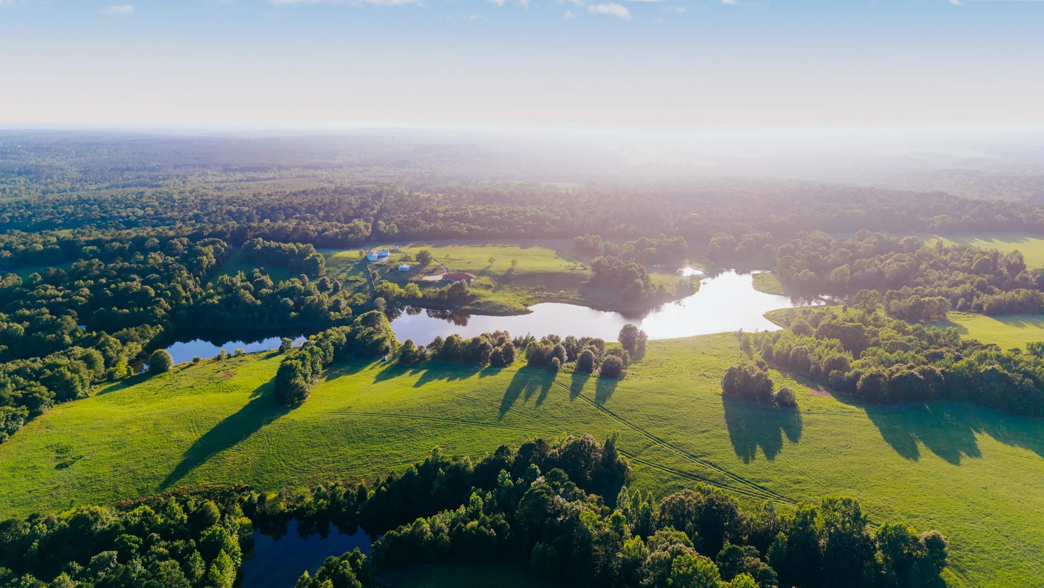 Expansive landscape featuring multiple bodies of water, verdant open fields, and mature tree lines