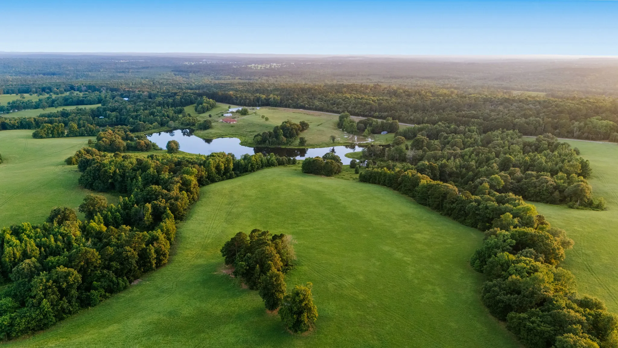 Expansive green pastures featuring mature trees and a tranquil pond