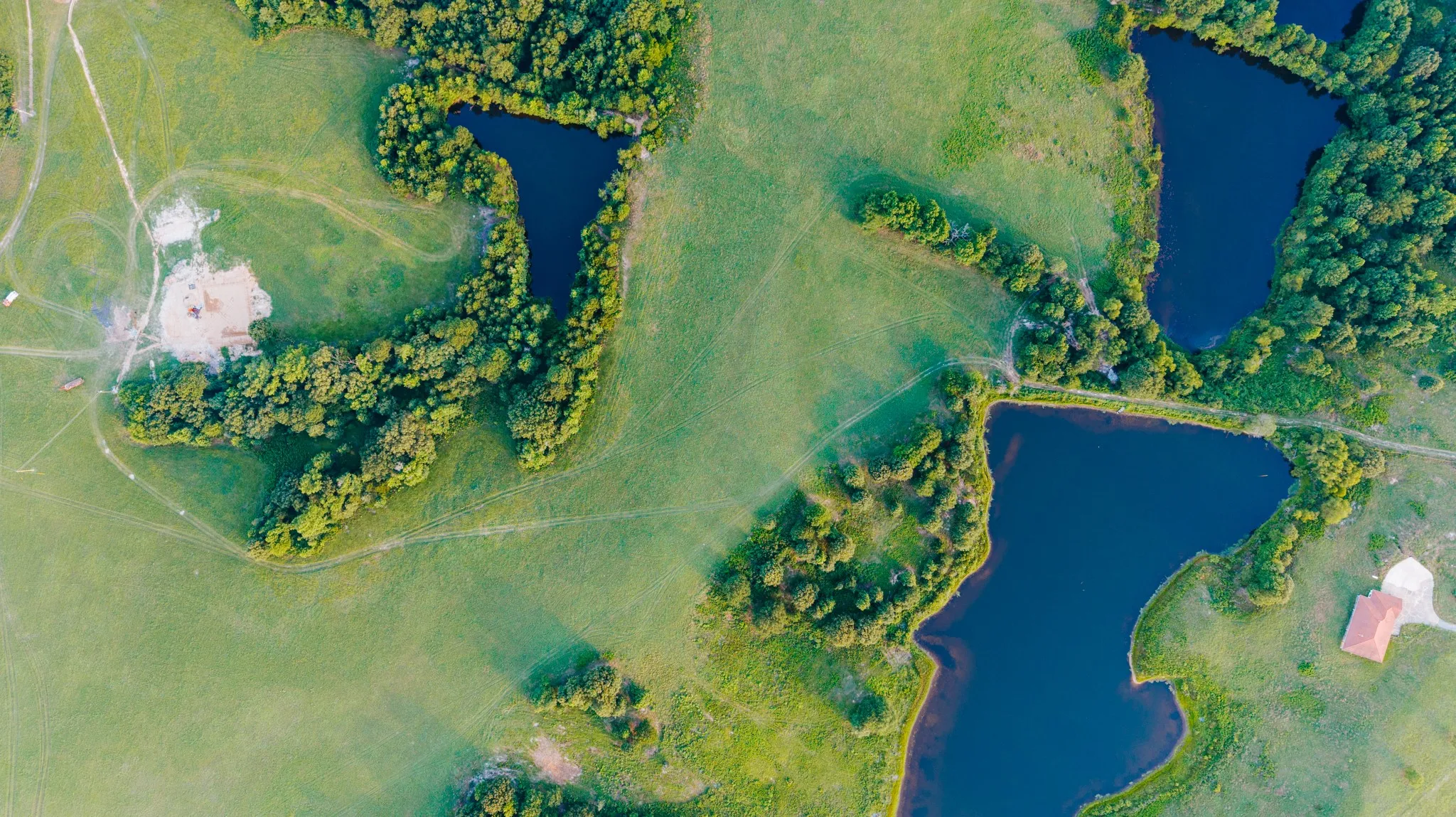 Expansive green landscape featuring multiple bodies of water, dense tree lines, and open grassy areas