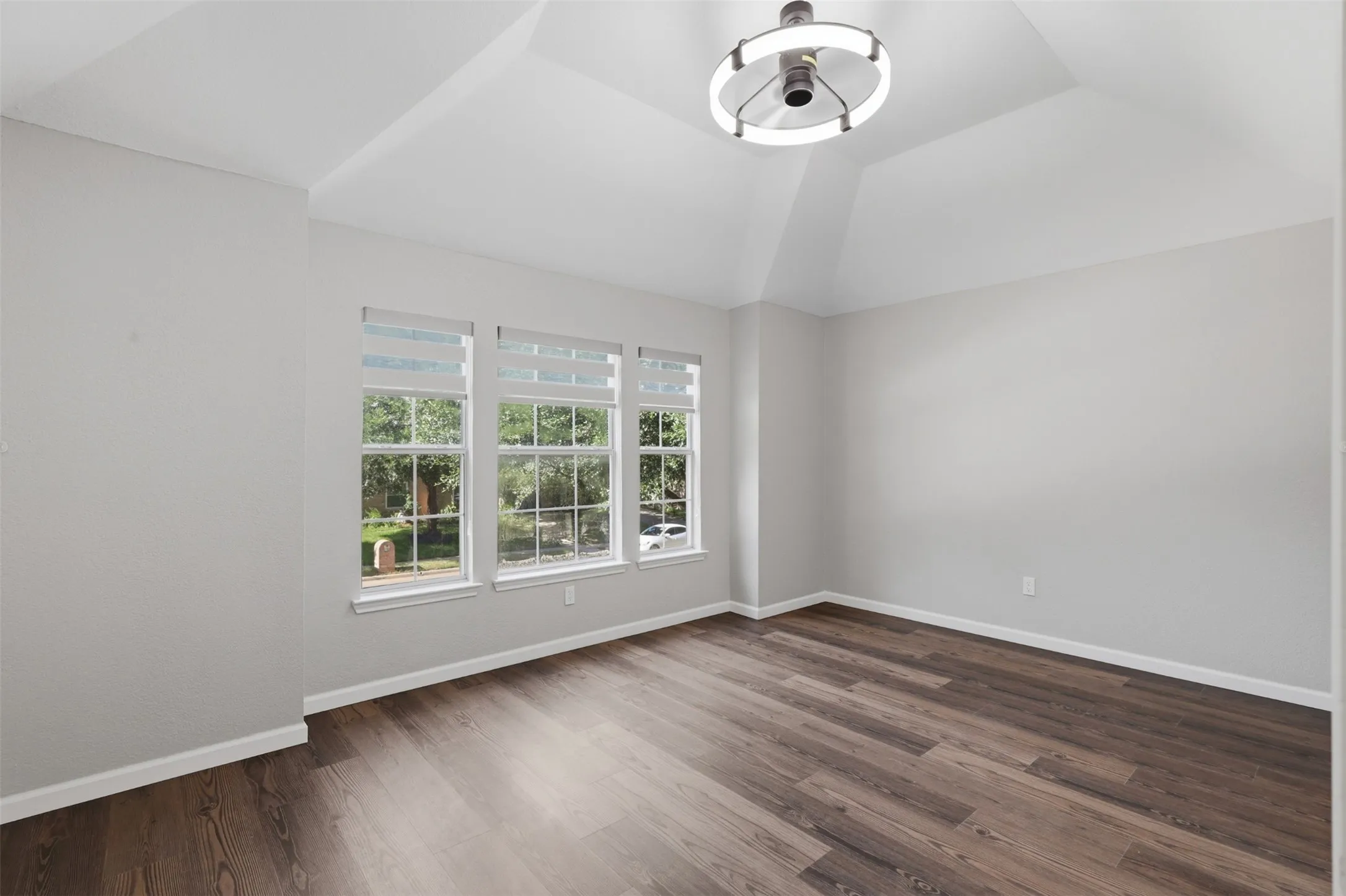 Spacious room featuring wood-finish flooring, vaulted ceilings, and a contemporary ceiling light fixture