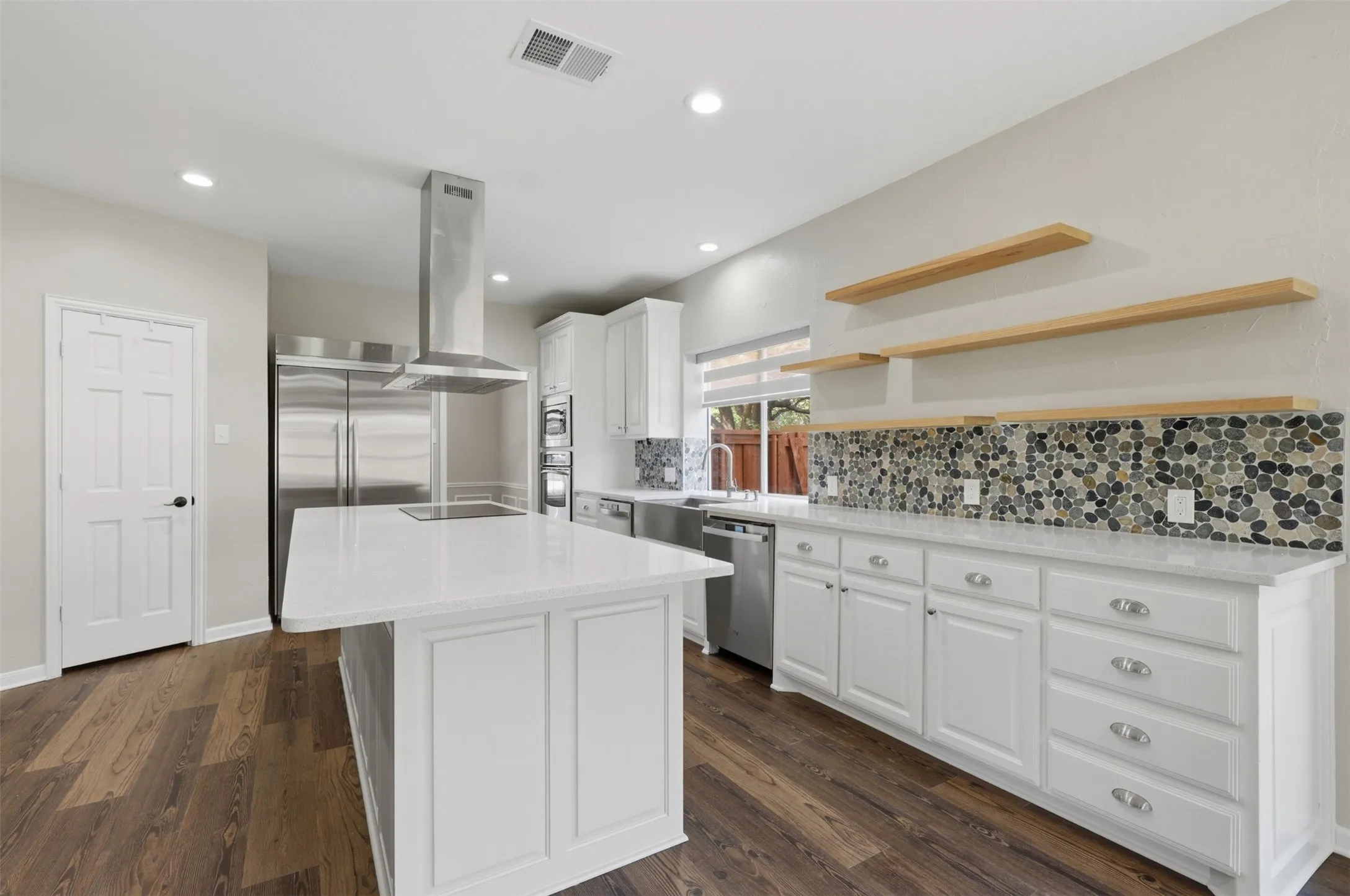 Kitchen featuring a center island with a white countertop, white cabinetry with silver hardware, stainless steel appliances, and wood-finish flooring