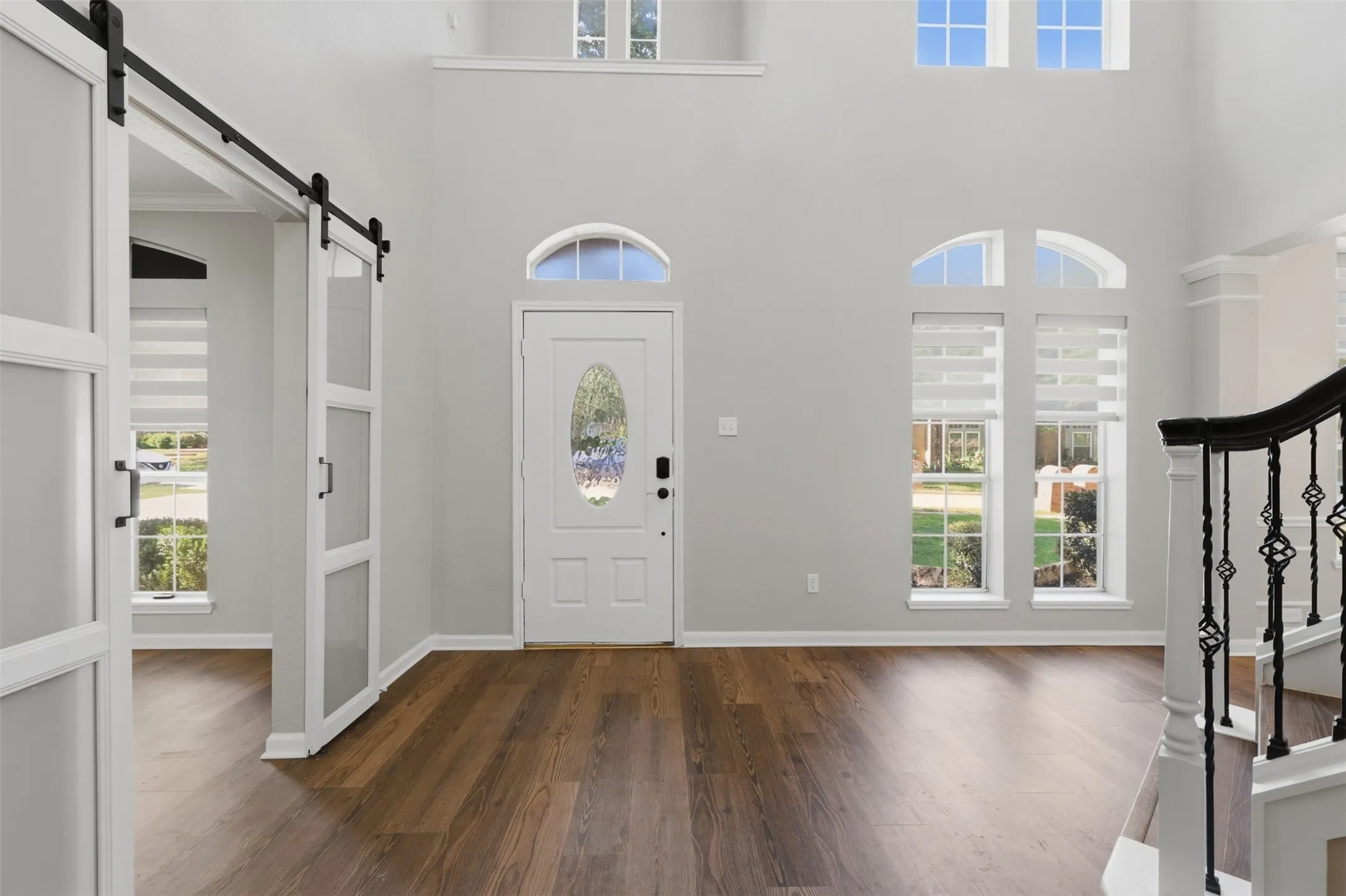 Two-story entryway featuring wood-finish flooring, a decorative front door with an oval glass insert, and a white barn door