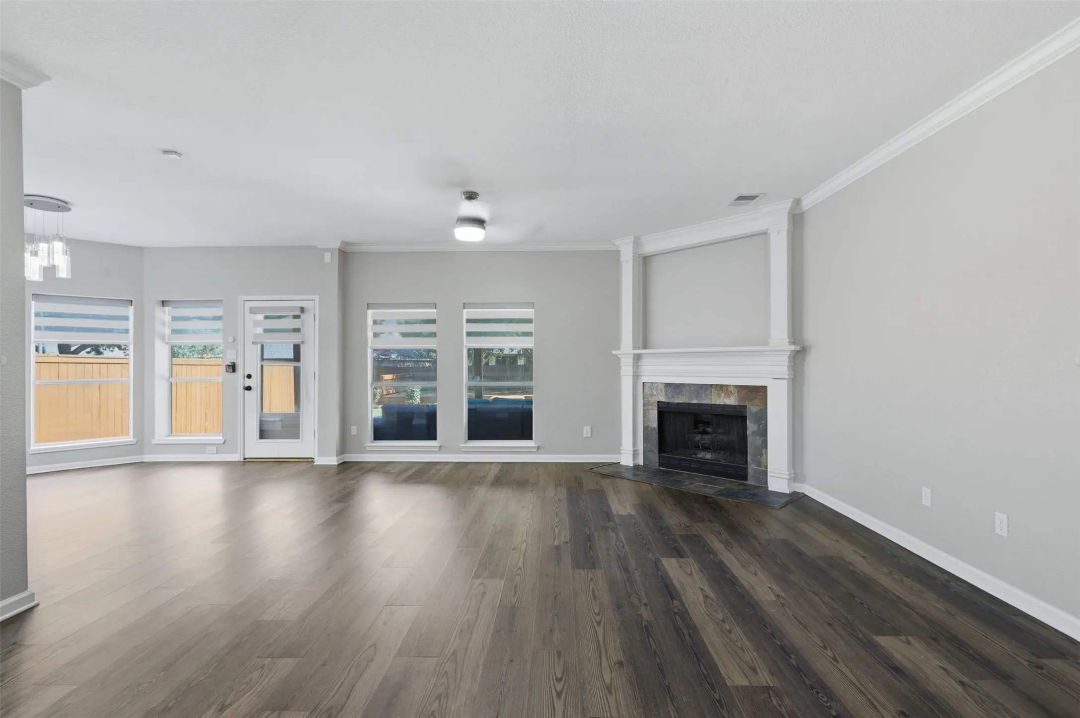 Spacious living area featuring wood-finish flooring, a corner fireplace with a stone surround, and multiple windows with blinds