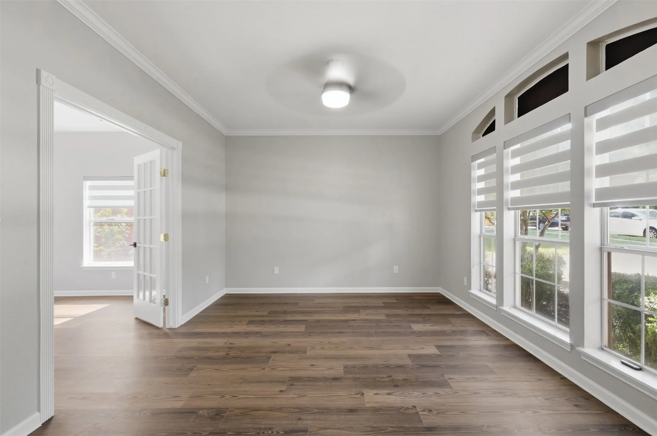 Spacious room featuring wood-finish flooring, light grey walls, and extensive crown molding