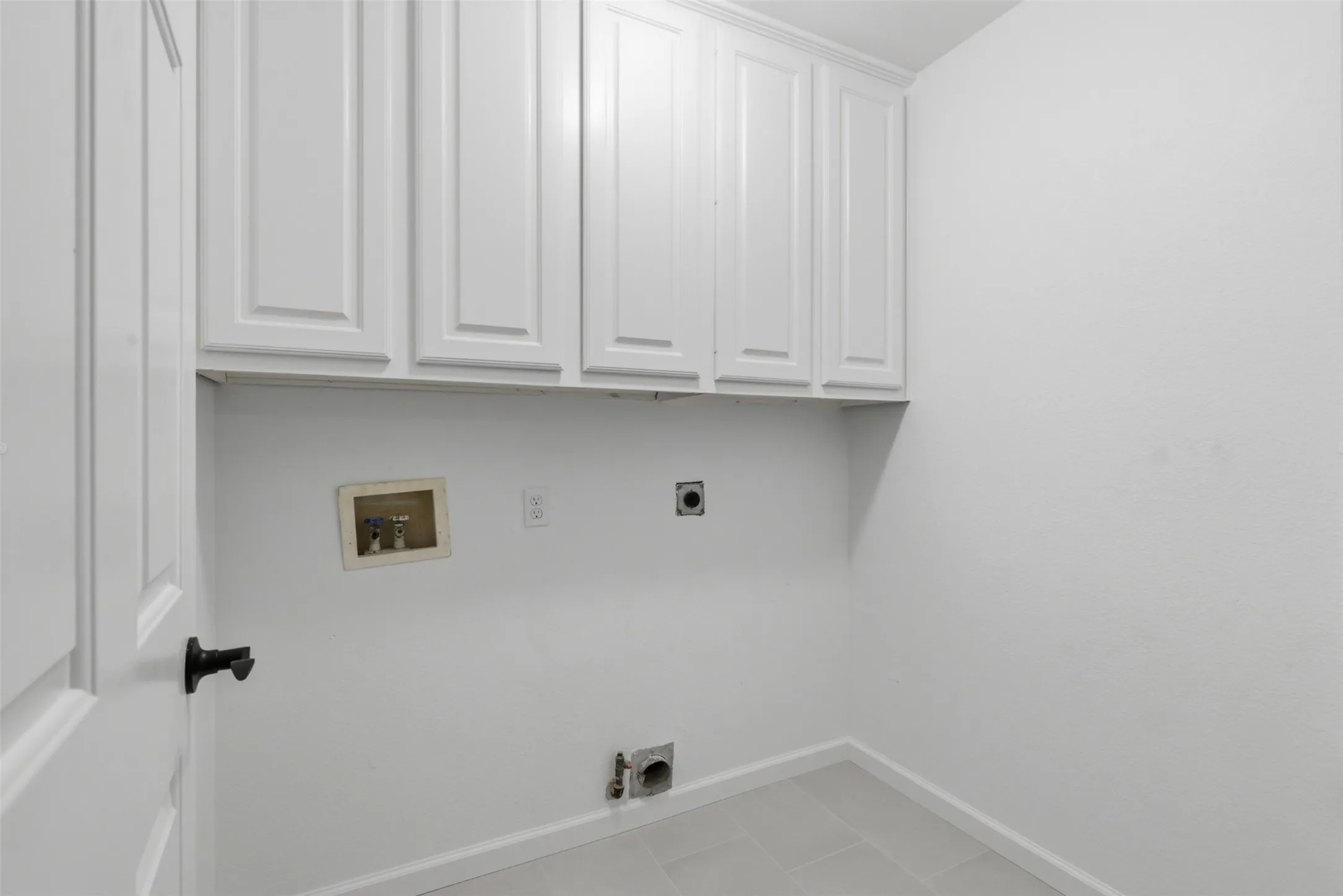 White shaker-style cabinetry providing storage, light grey tiled flooring, and white walls