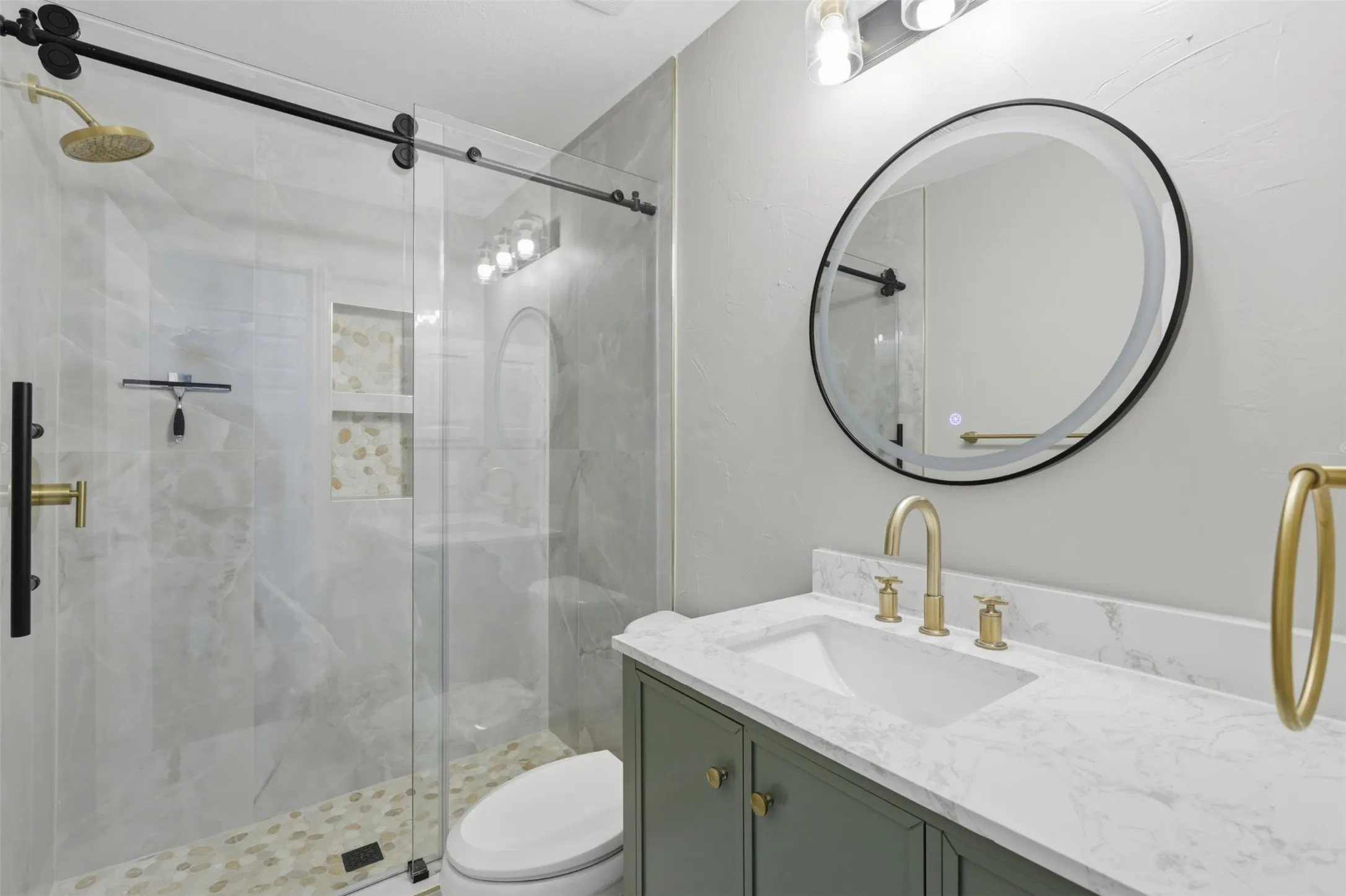 Modern bathroom featuring a frameless glass shower enclosure with a sliding barn door system, a rainfall showerhead, and pebble tile flooring