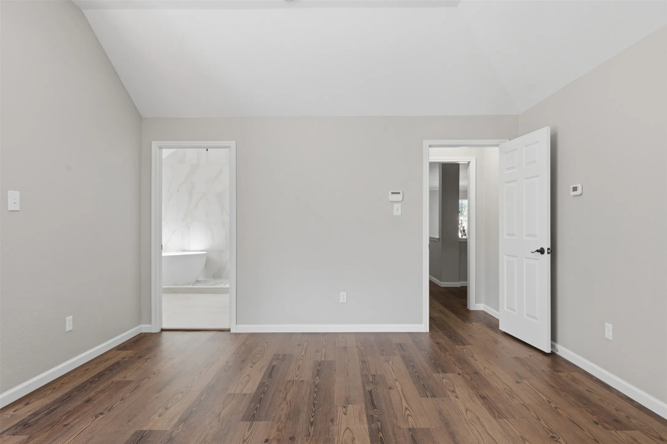 Spacious interior room featuring wood-finish flooring, vaulted ceilings, and light gray wall paint