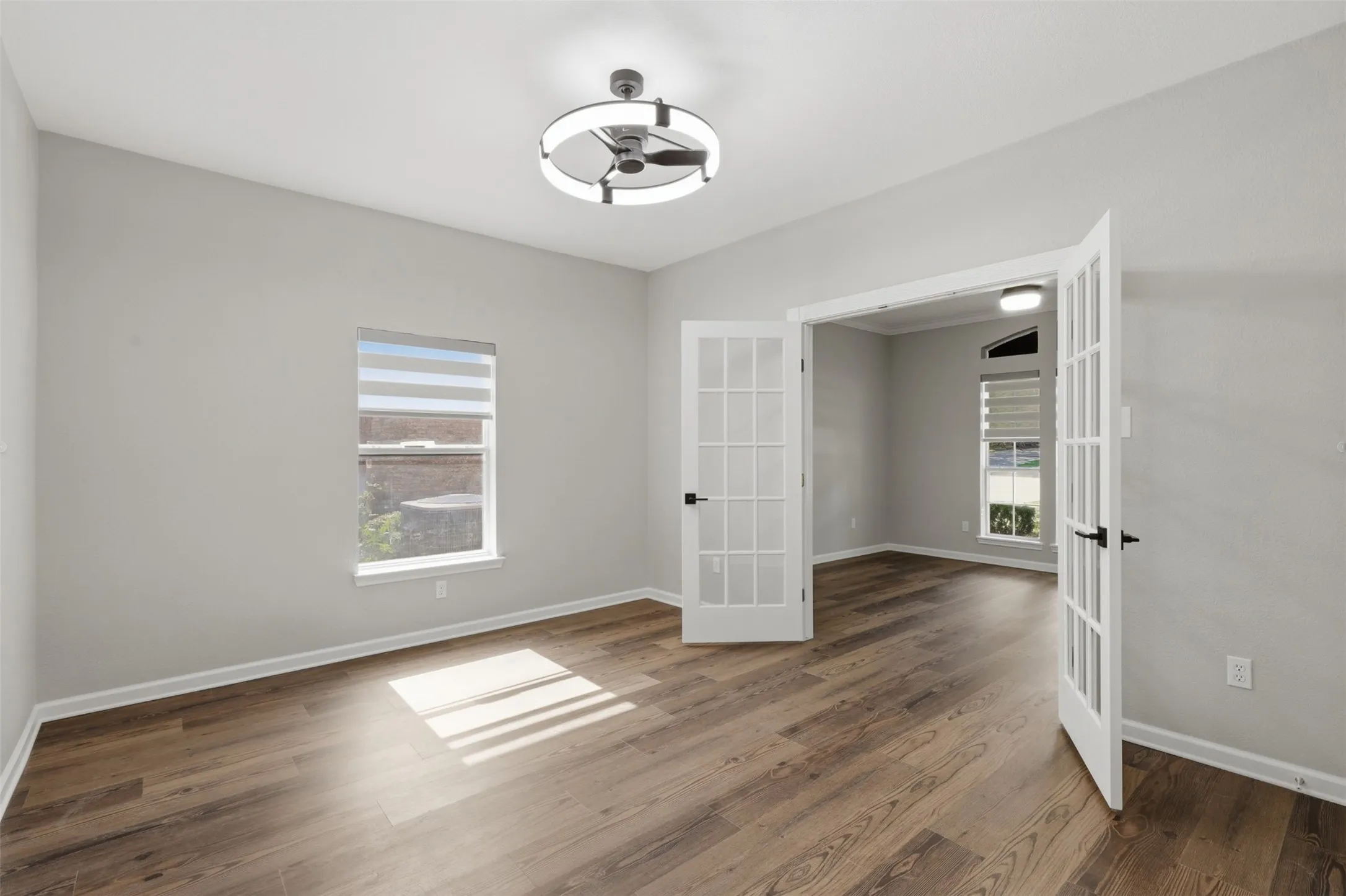 Spacious room featuring wood-finish flooring, light grey walls, and a contemporary ceiling fan with integrated lighting