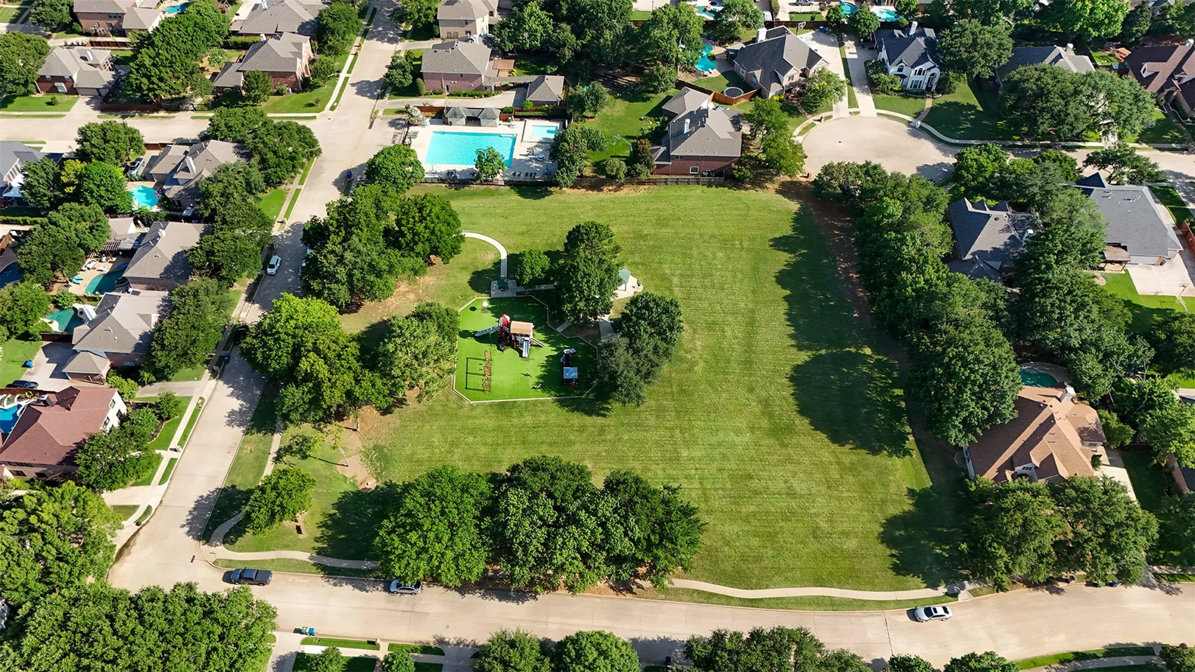 Expansive green space featuring mature trees, a walking path, and recreational equipment