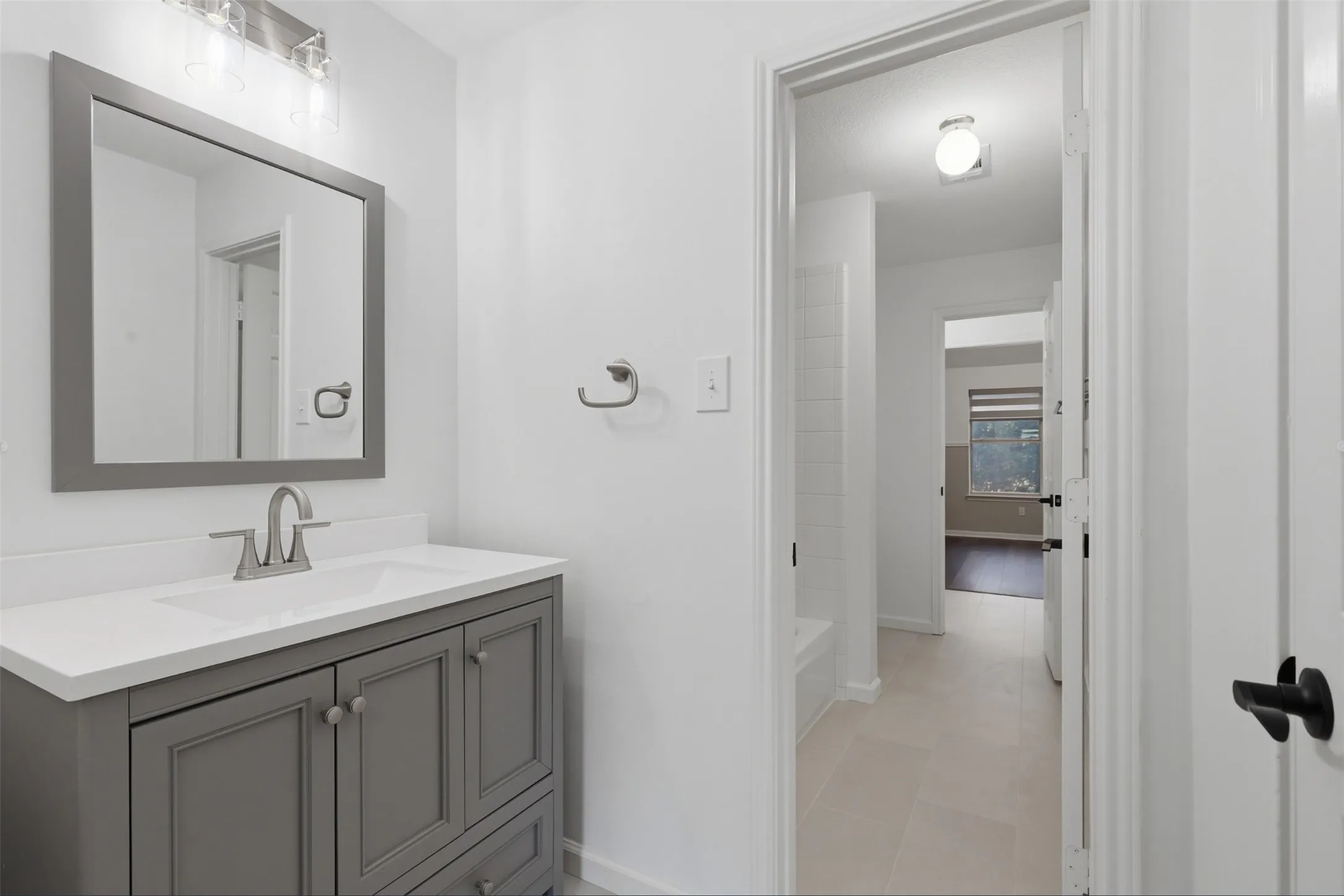 Bathroom vanity featuring a grey cabinet, white countertop with integrated sink, brushed nickel faucet, and framed​​‌​​​​‌​​‌‌​‌‌​​​‌‌​‌​‌​‌​​​‌​​ mirror