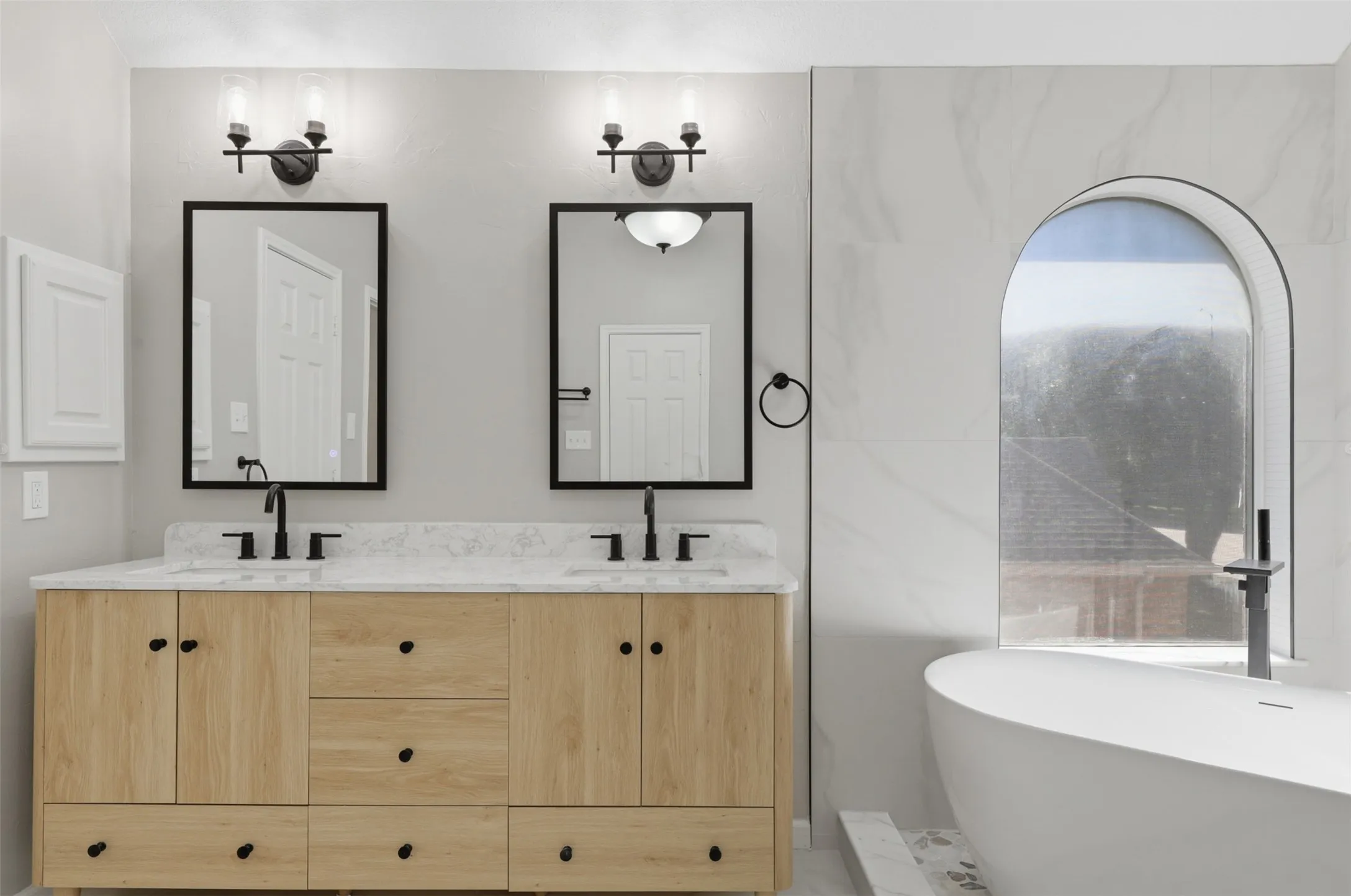 Dual vanity with natural wood-finish cabinetry, white stone countertops, and matte black fixtures