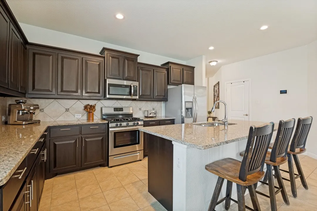 Kitchen featuring granite countertops, dark wood-finish cabinetry, stainless steel appliances, a tiled backsplash, and recessed lighting