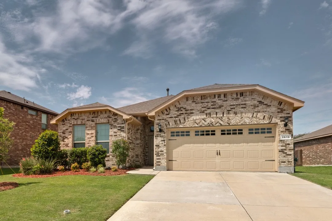 Single-story brick exterior featuring a two-car garage with decorative hardware, a concrete driveway, and a manicured lawn with mature shrubs