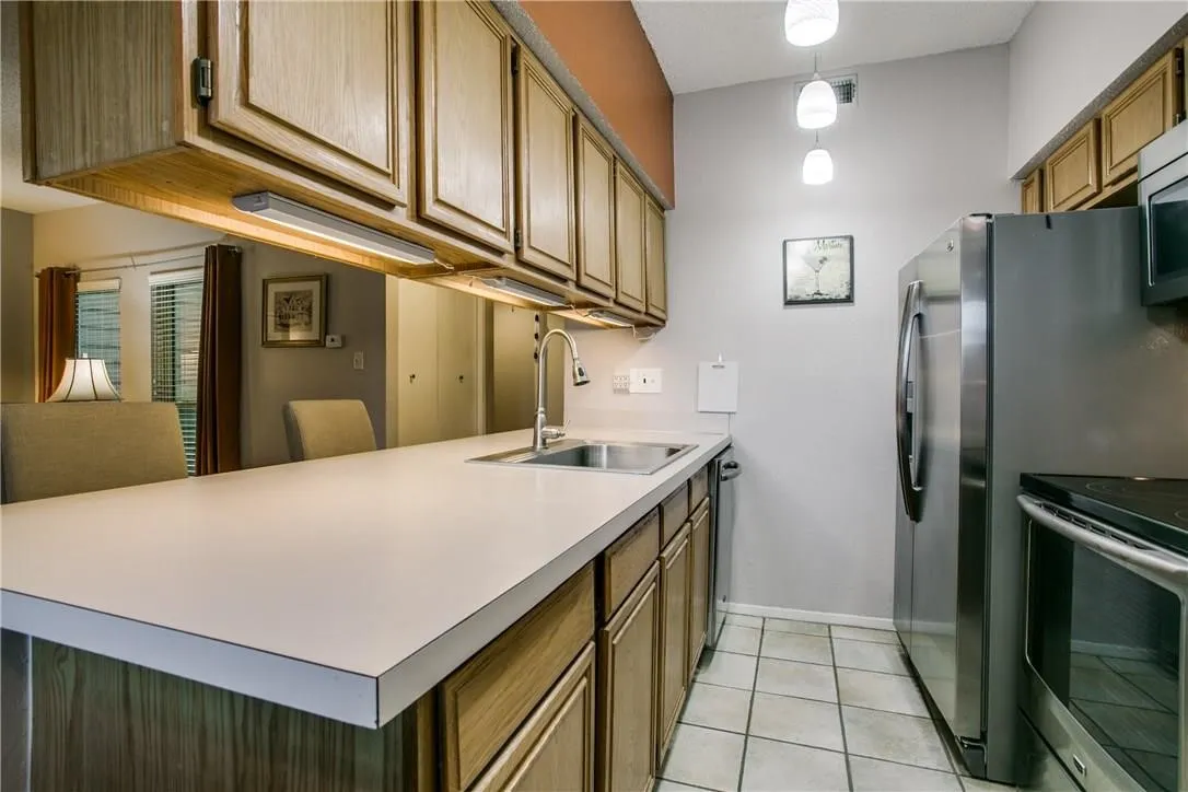 Kitchen with light tile flooring, sink, appliances with stainless steel finishes, and decorative light fixtures