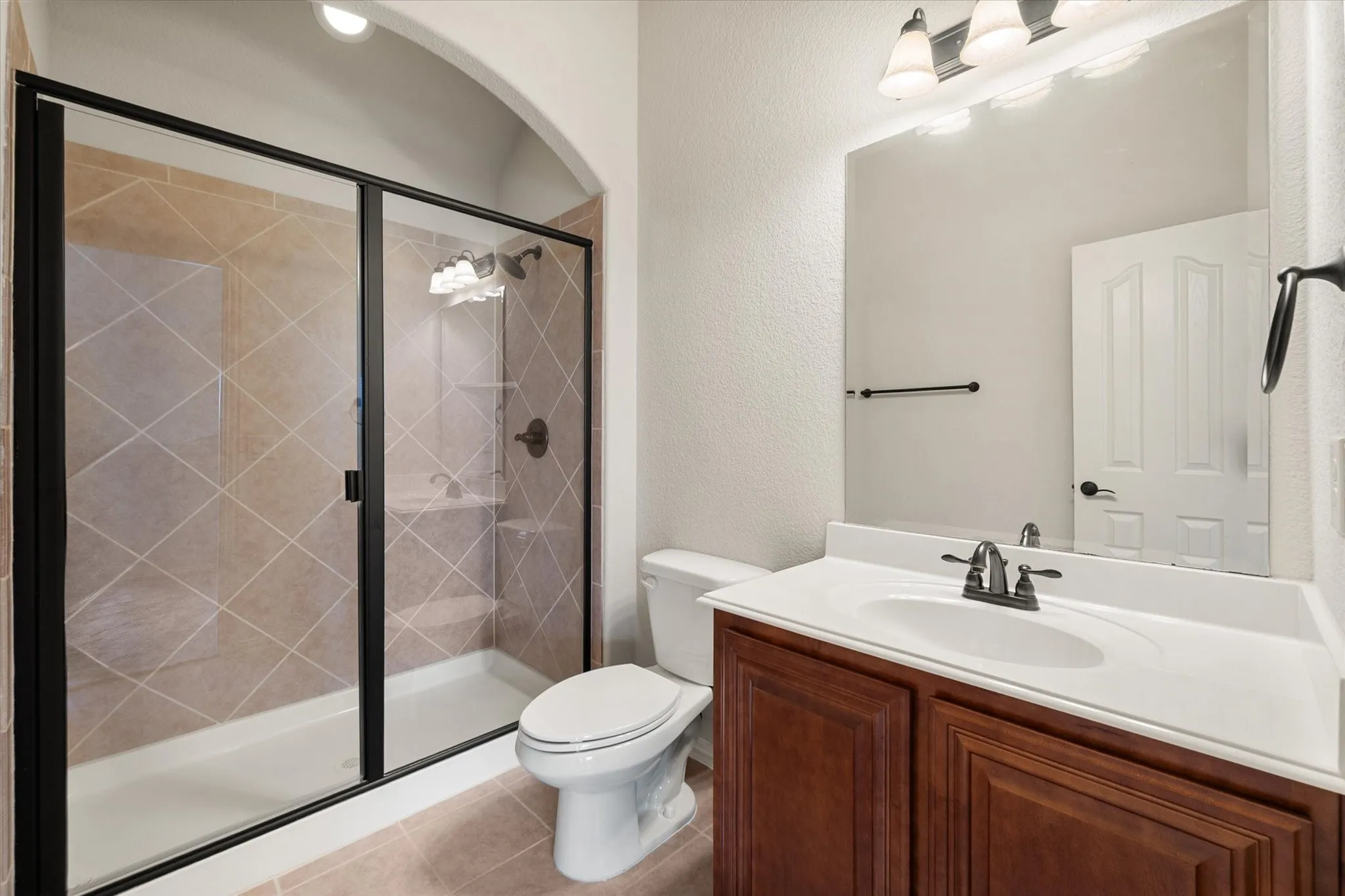 Full bathroom featuring a shower with dark bronze framed glass enclosure, diagonal tile surround, built-in shelving, and dark bronze fixtures