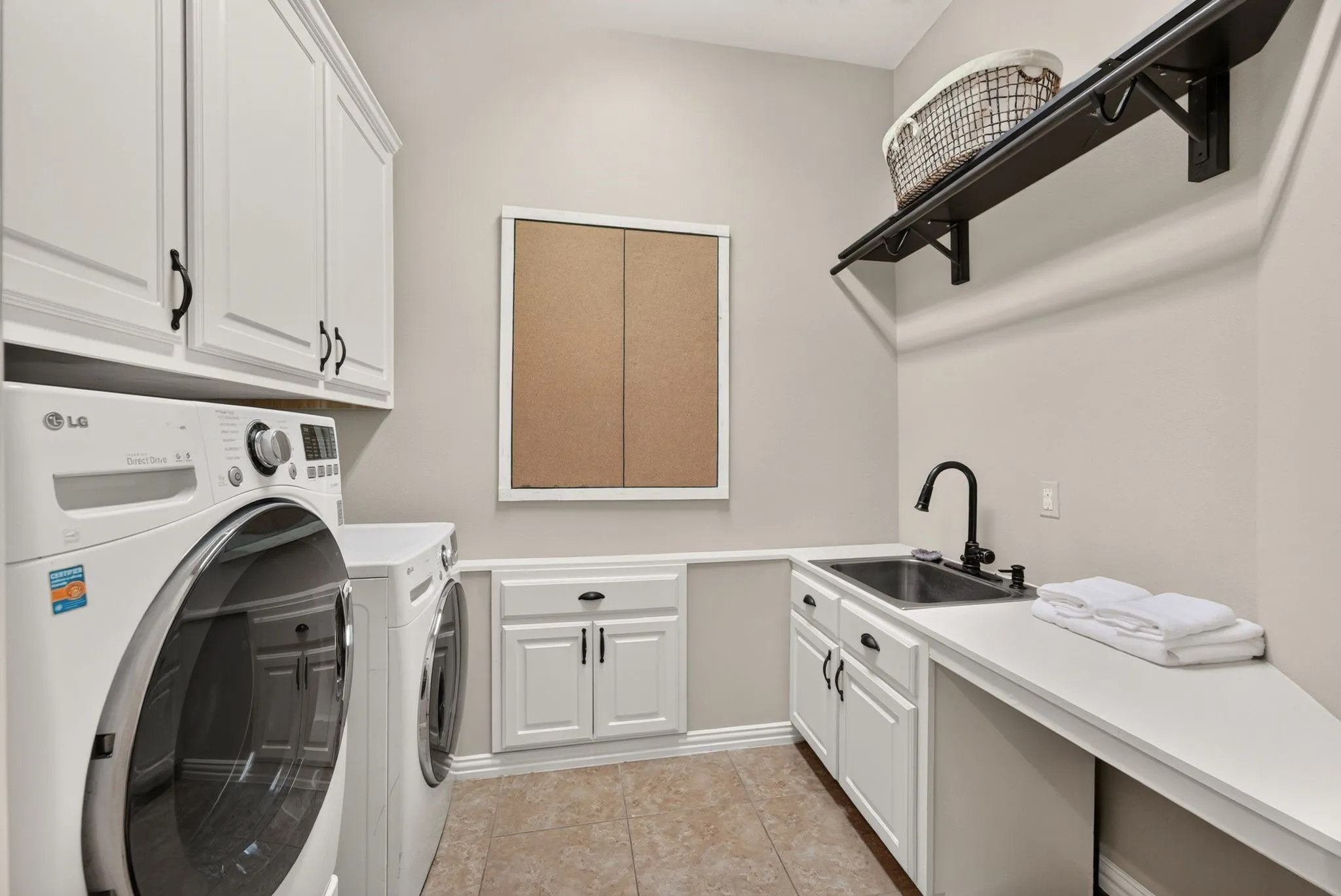 White cabinetry, durable tiled flooring, utility sink with black faucet, built-in shelving, and white countertops
