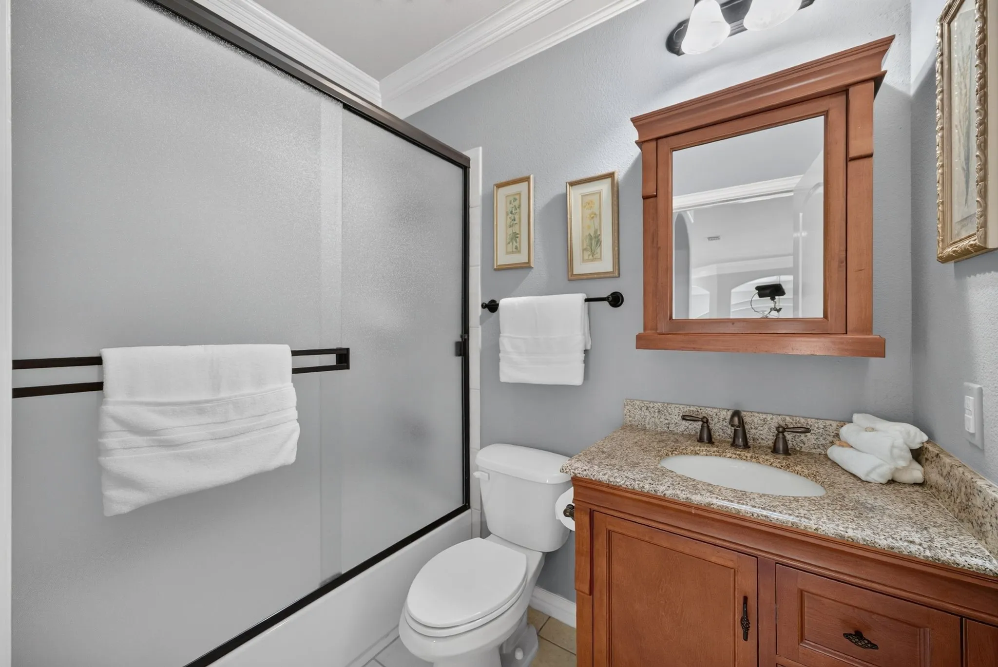 Bathroom featuring a frosted glass shower enclosure, a wood-finish vanity with a granite-style countertop, an undermount sink, and a framed mirror