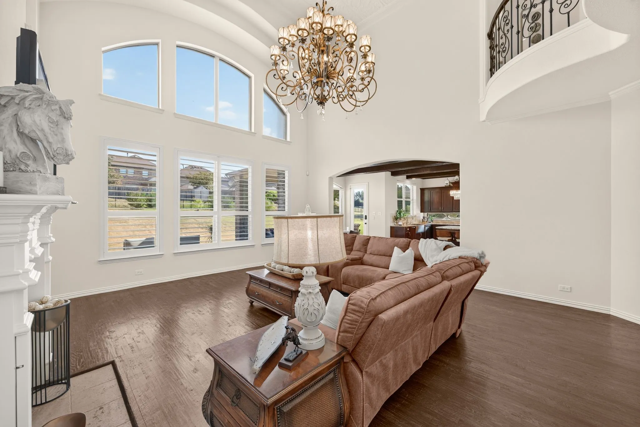 Two-story great room with a tiered chandelier, arched transom windows, and wood-finish flooring