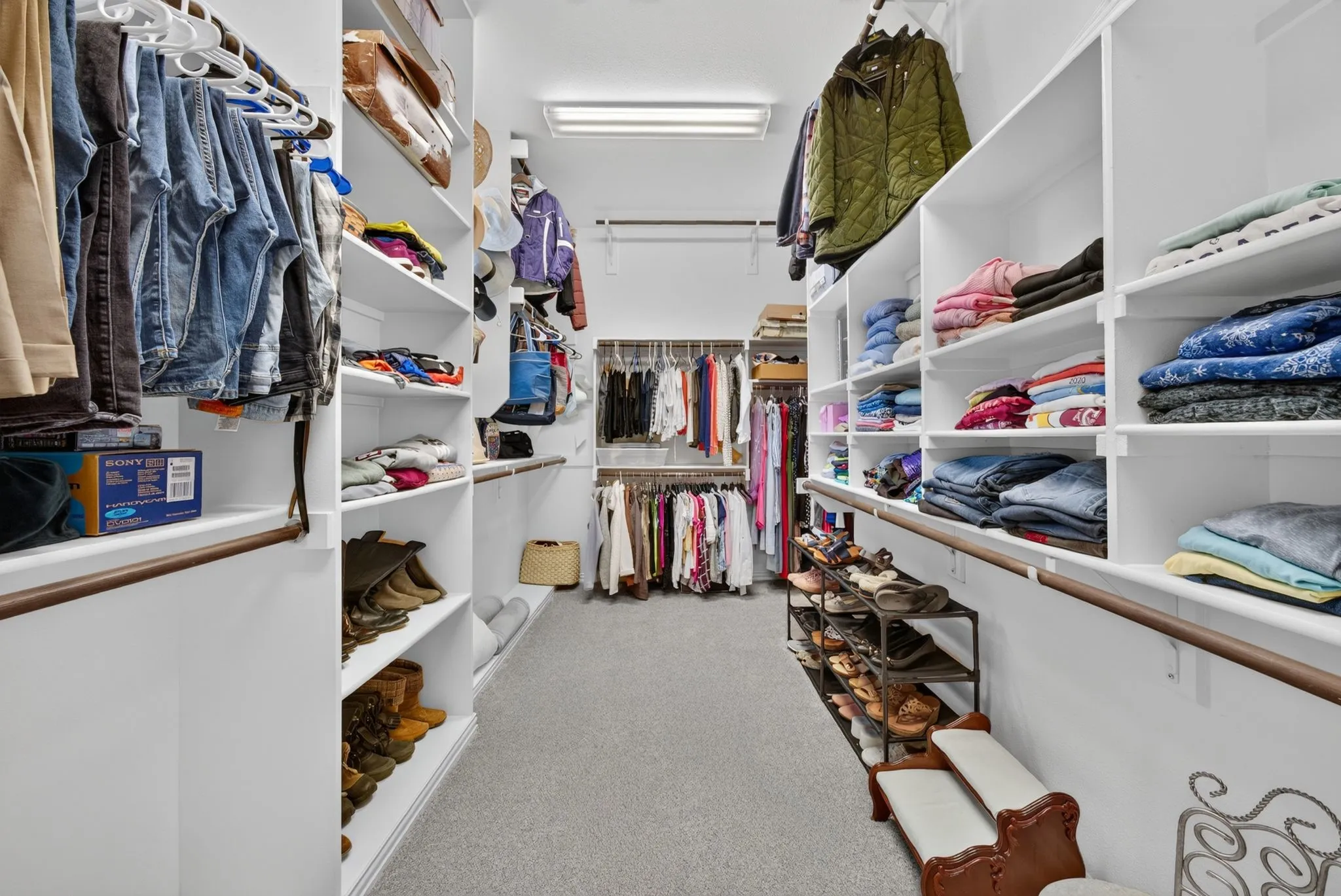 Spacious walk-in closet featuring extensive built-in shelving, multiple hanging rods, and recessed lighting