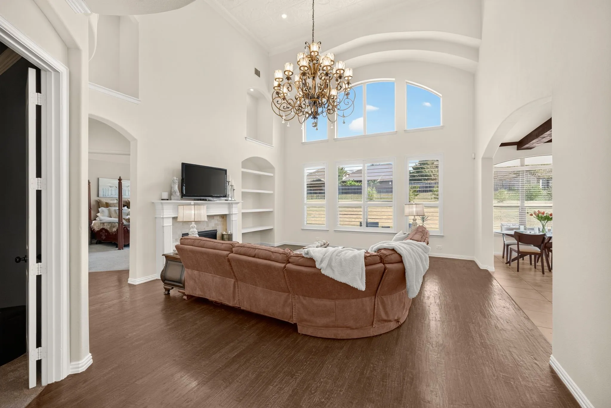 Vaulted ceilings with architectural archways, prominent chandelier, and wood-finish flooring