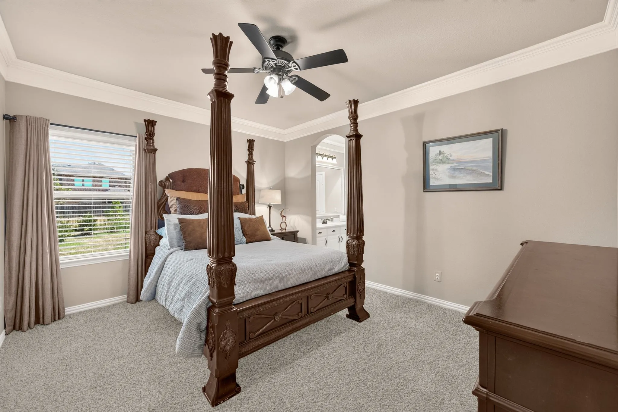 Tray ceiling with crown molding, ceiling fan, carpet flooring, window with blinds, and an arched entry to an adjoining space