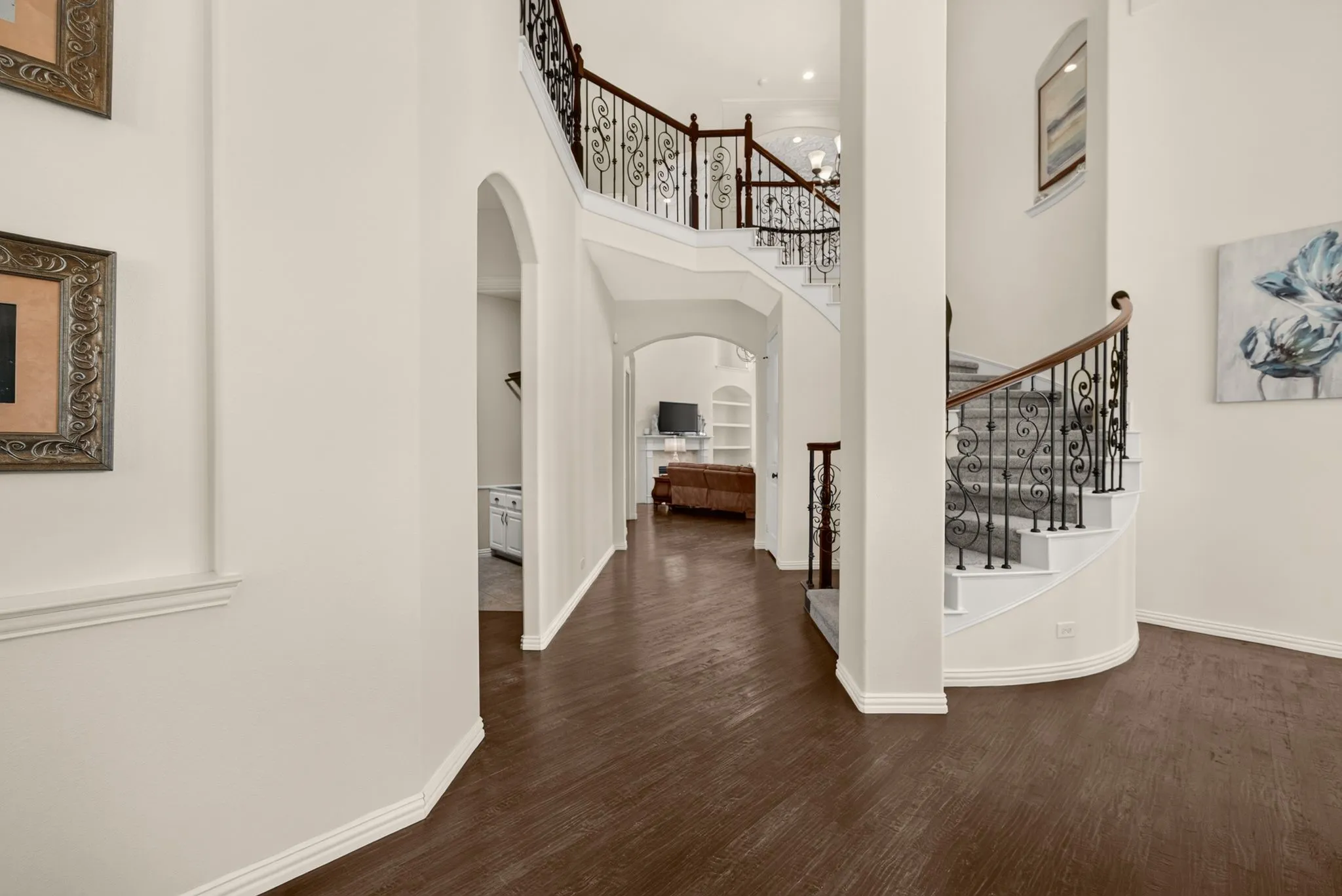 Grand entry featuring dark wood-finish flooring, a curved staircase with wrought iron balusters, and arched doorways