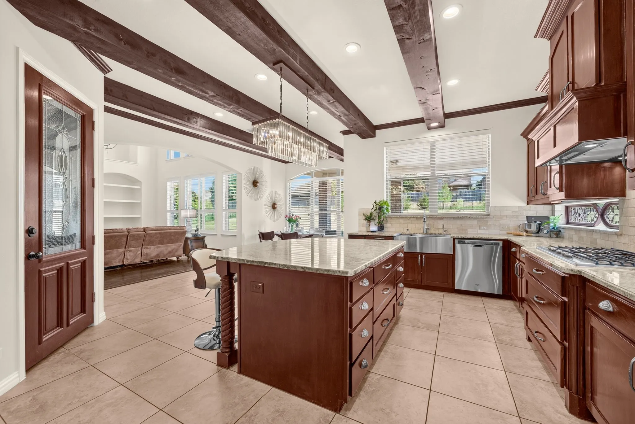 Kitchen featuring exposed wood beams, a large central island with a granite countertop, wood cabinetry, stainless steel appliances, and tile flooring
