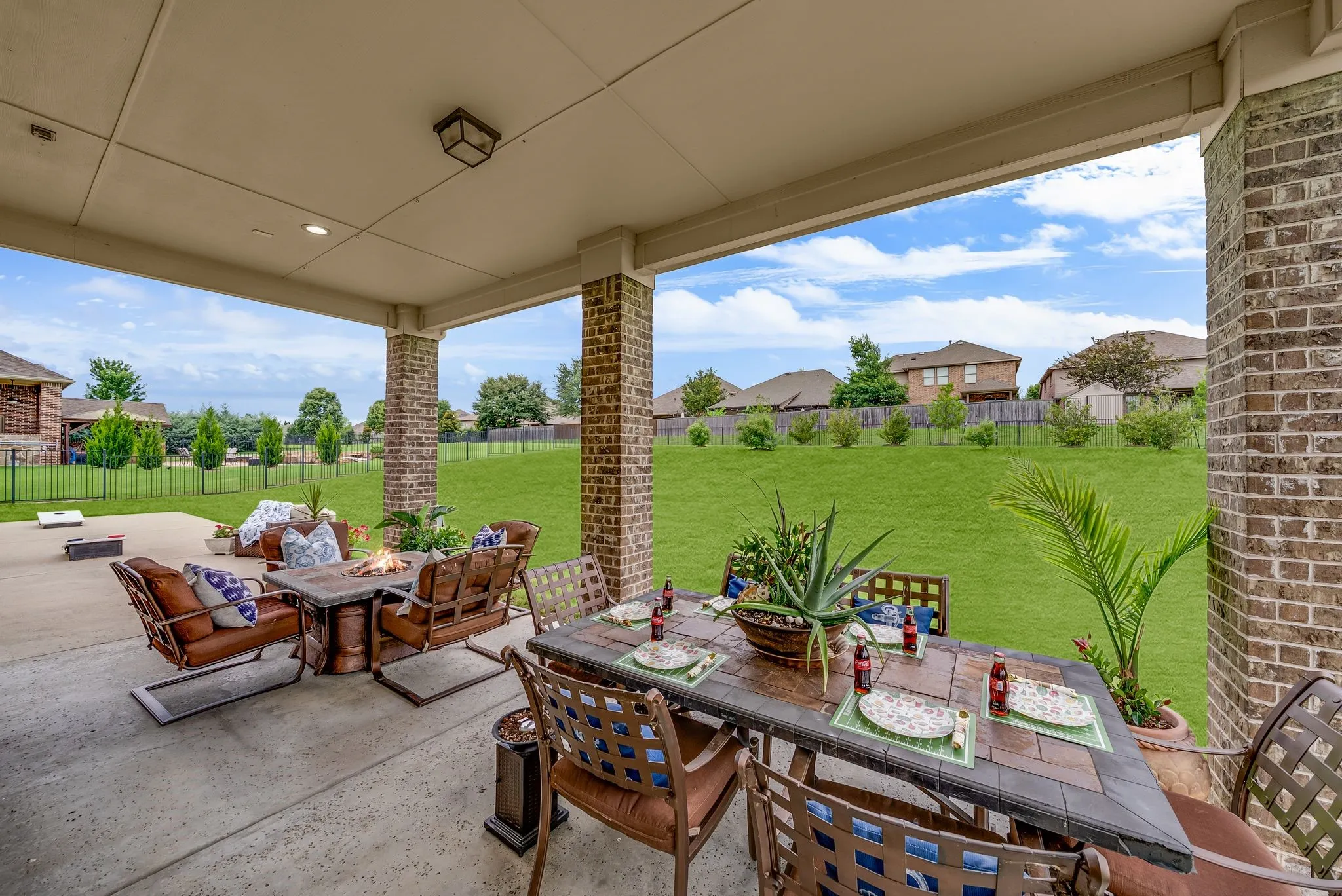 Covered concrete patio featuring brick columns, recessed lighting, and a spacious green lawn