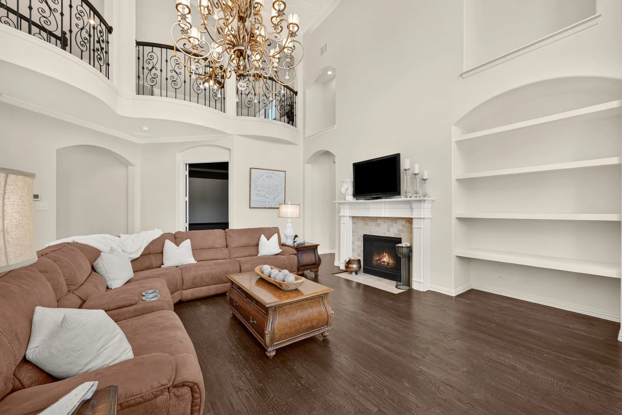 Two-story living area featuring a fireplace with a stone surround, built-in shelving, wood-finish flooring, and a wrought iron balcony
