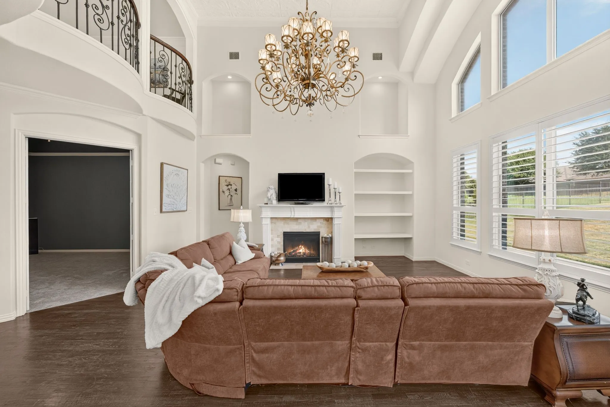 Two-story living area featuring a decorative chandelier, fireplace with stone surround, built-in shelving, wood-finish flooring, and arched entryways
