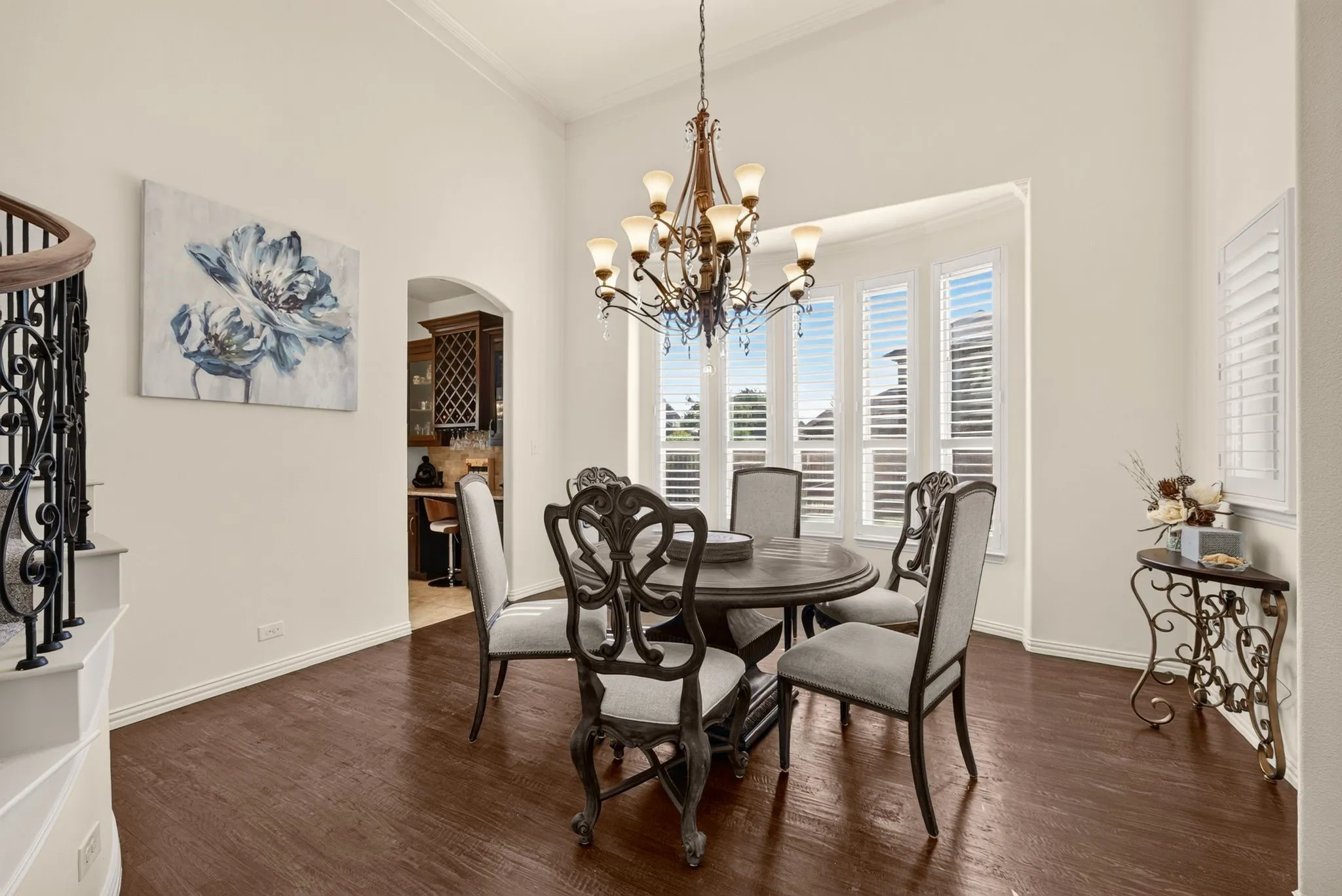 Dining area with wood-finish flooring, a bay window featuring plantation shutters, and an ornate chandelier