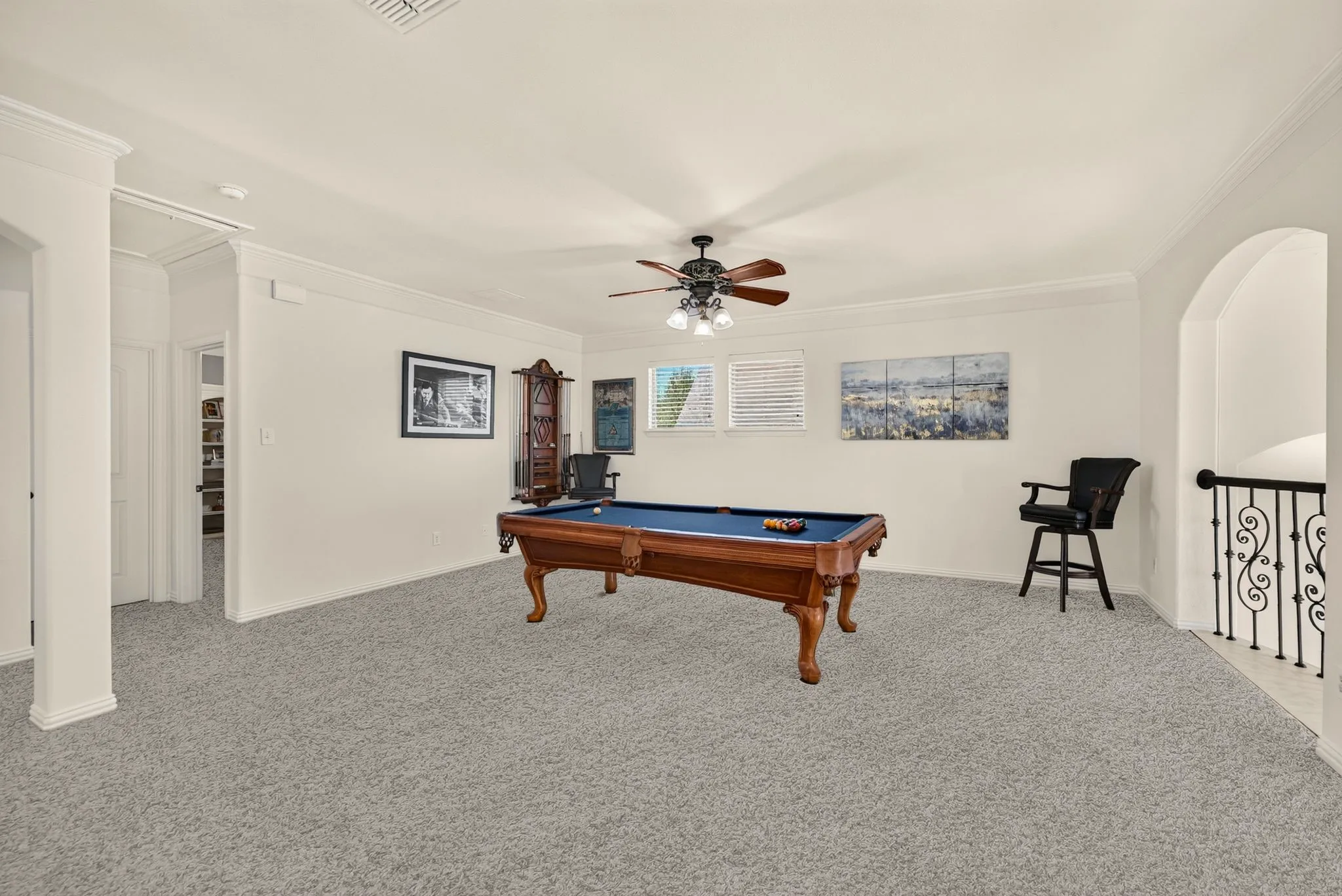 Carpeted room featuring crown molding, a ceiling fan with integrated lighting, and an arched entryway with decorative iron balusters