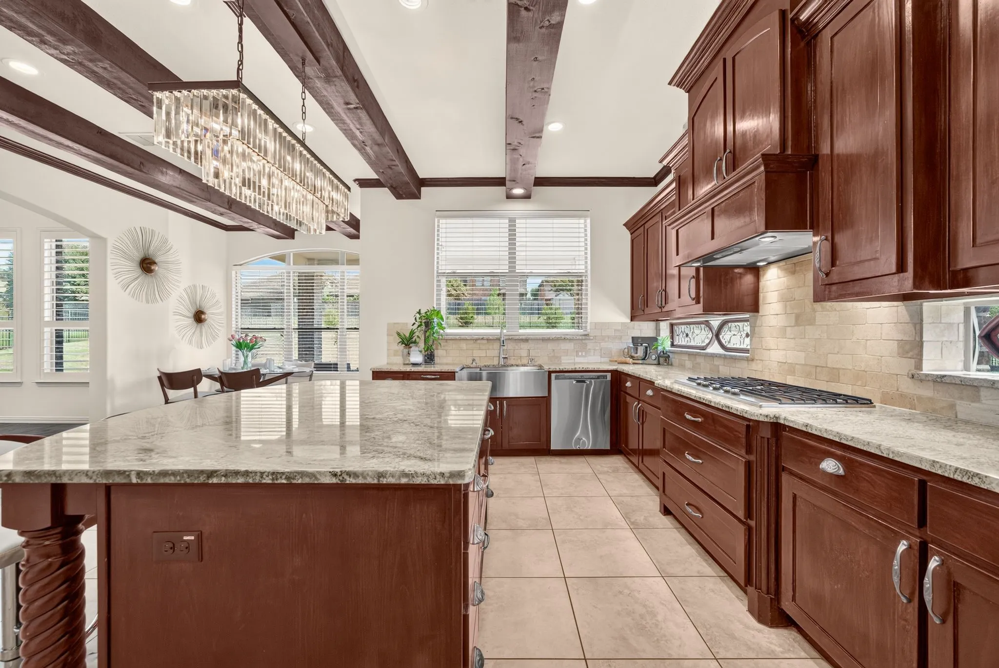 Spacious kitchen featuring rich wood cabinetry, stone countertops, a large island, stainless steel appliances, and ceiling beams