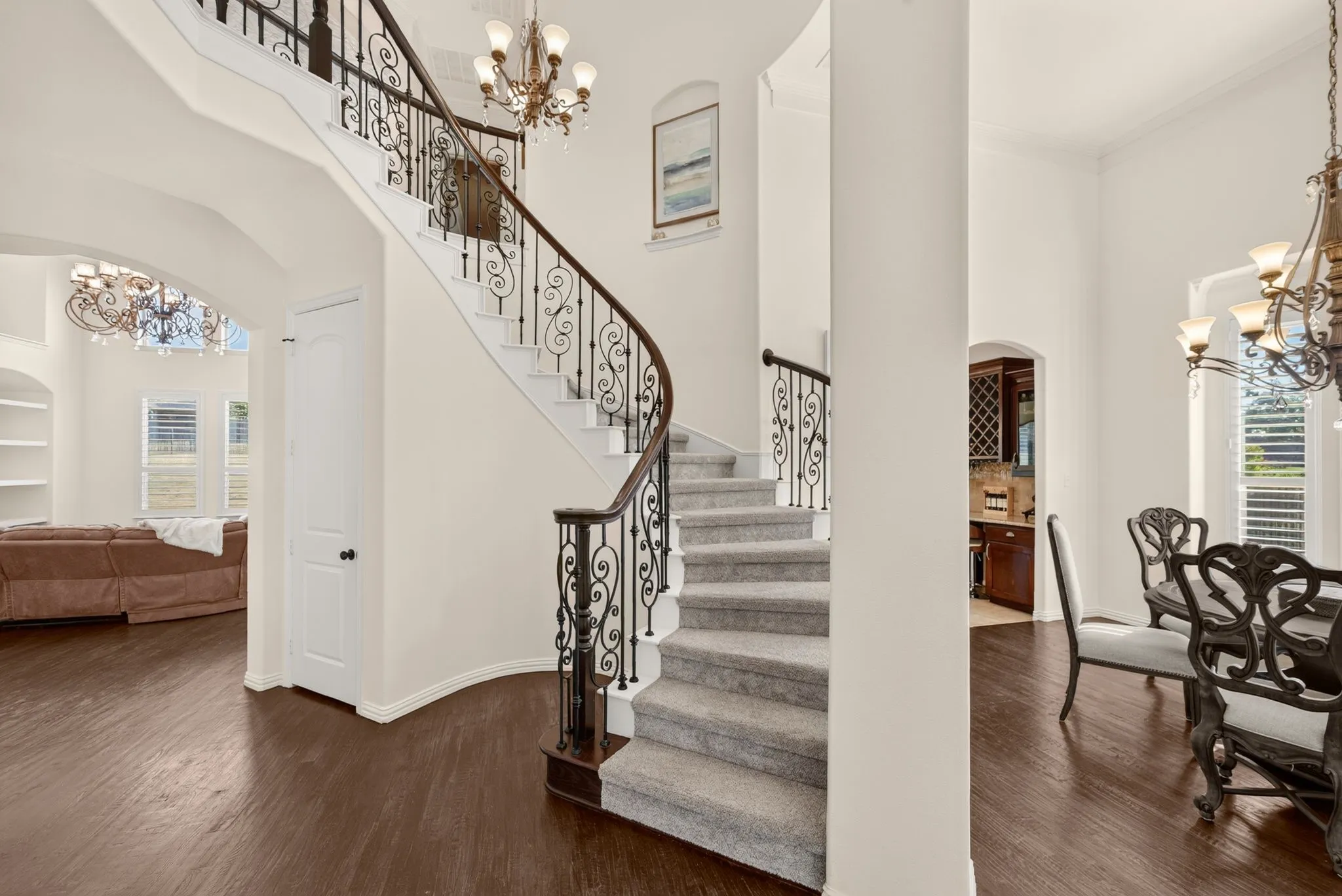 Curved staircase with wrought iron balusters, wood-finish flooring, and a chandelier lighting fixture