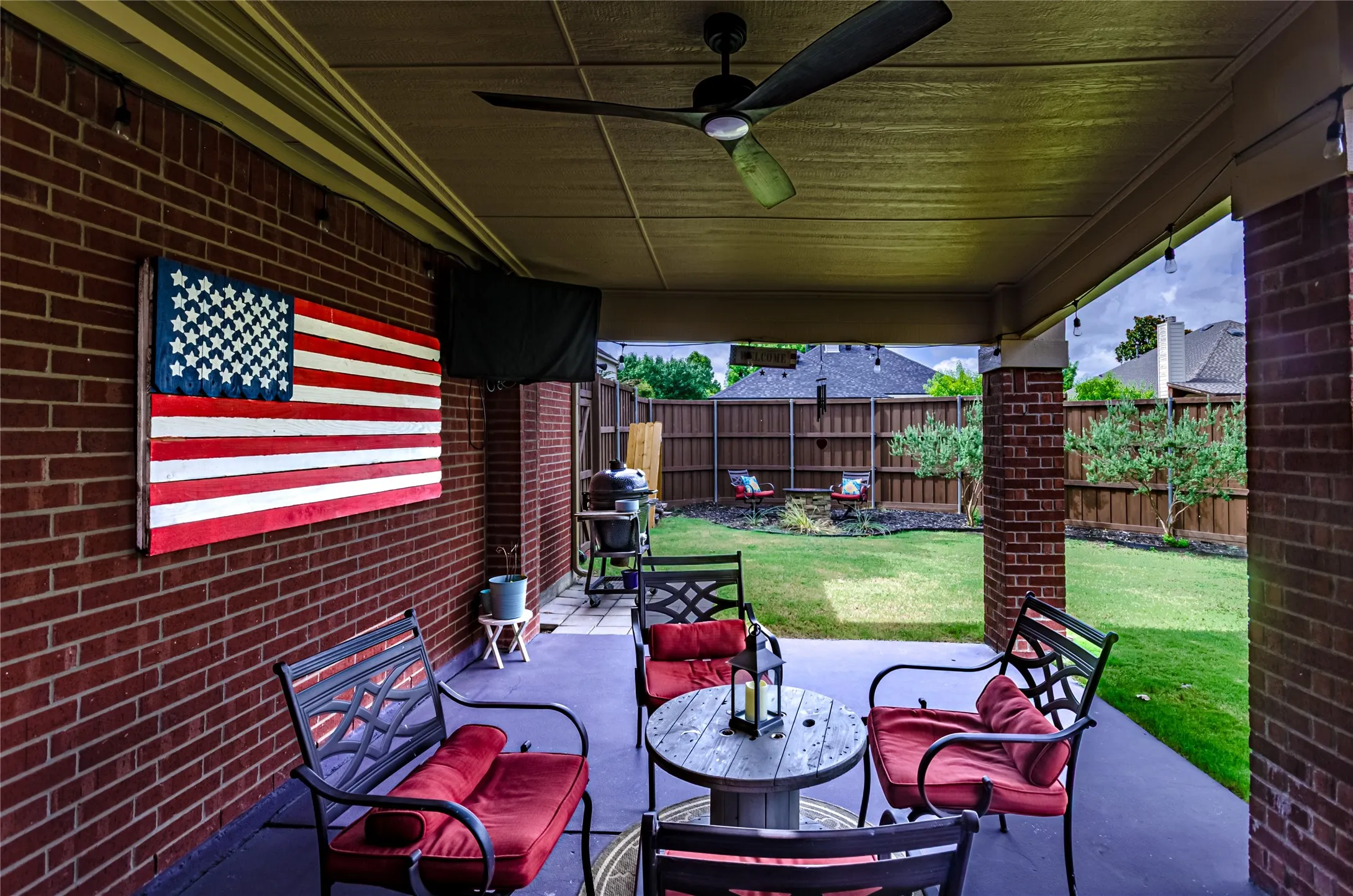 Covered patio featuring a ceiling fan, string lighting, and brick columns