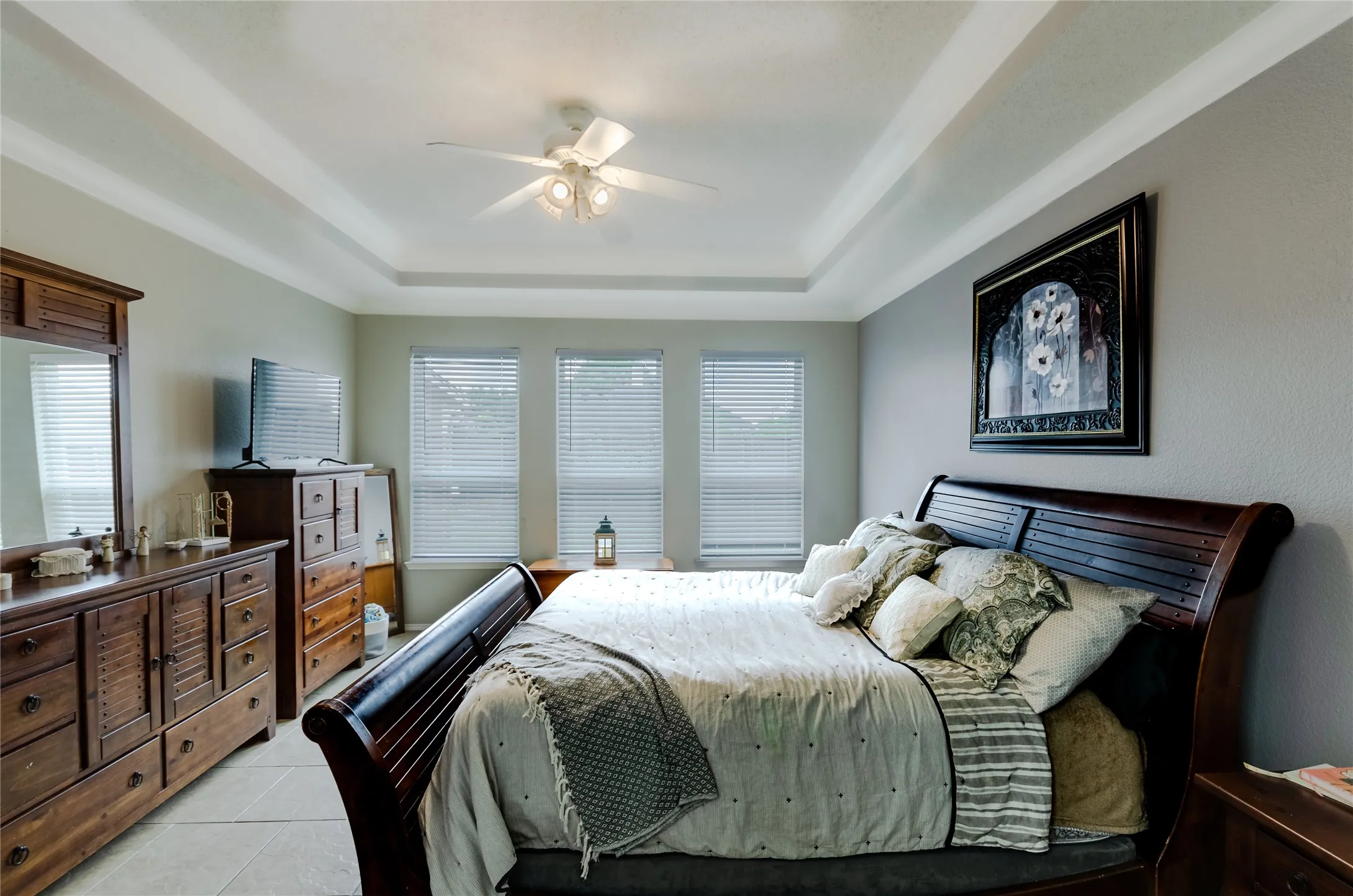 Spacious room featuring a tray ceiling, ceiling fan with integrated lighting, three windows with horizontal blinds, and neutral wall tones