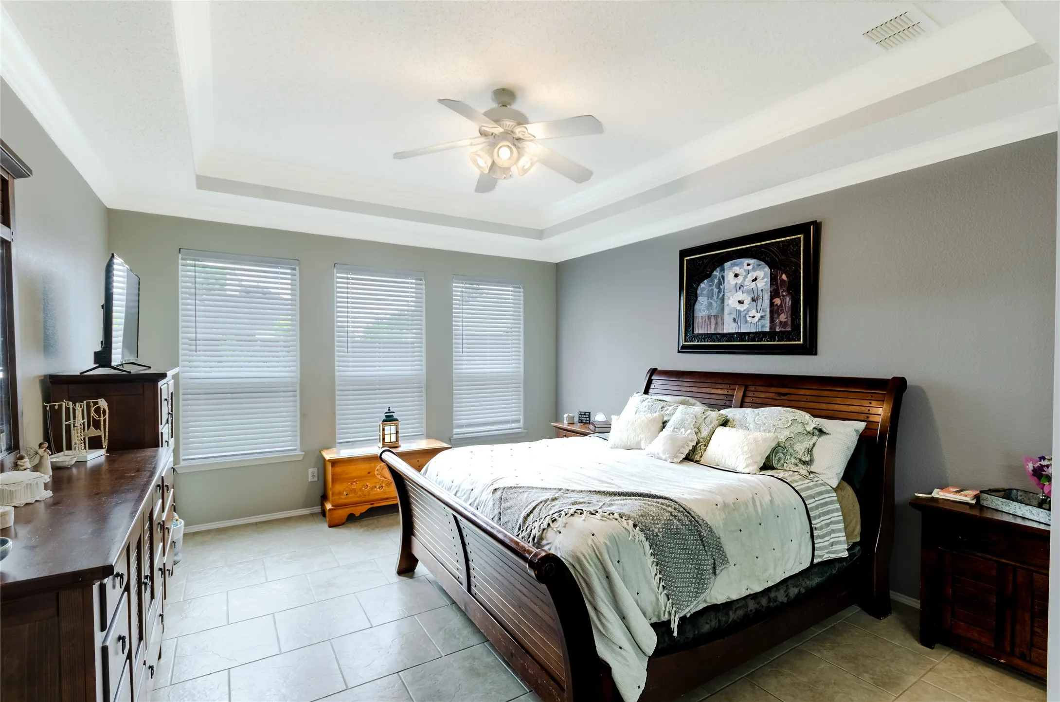 Room featuring a tray ceiling with crown molding and ceiling fan, three windows with blinds
